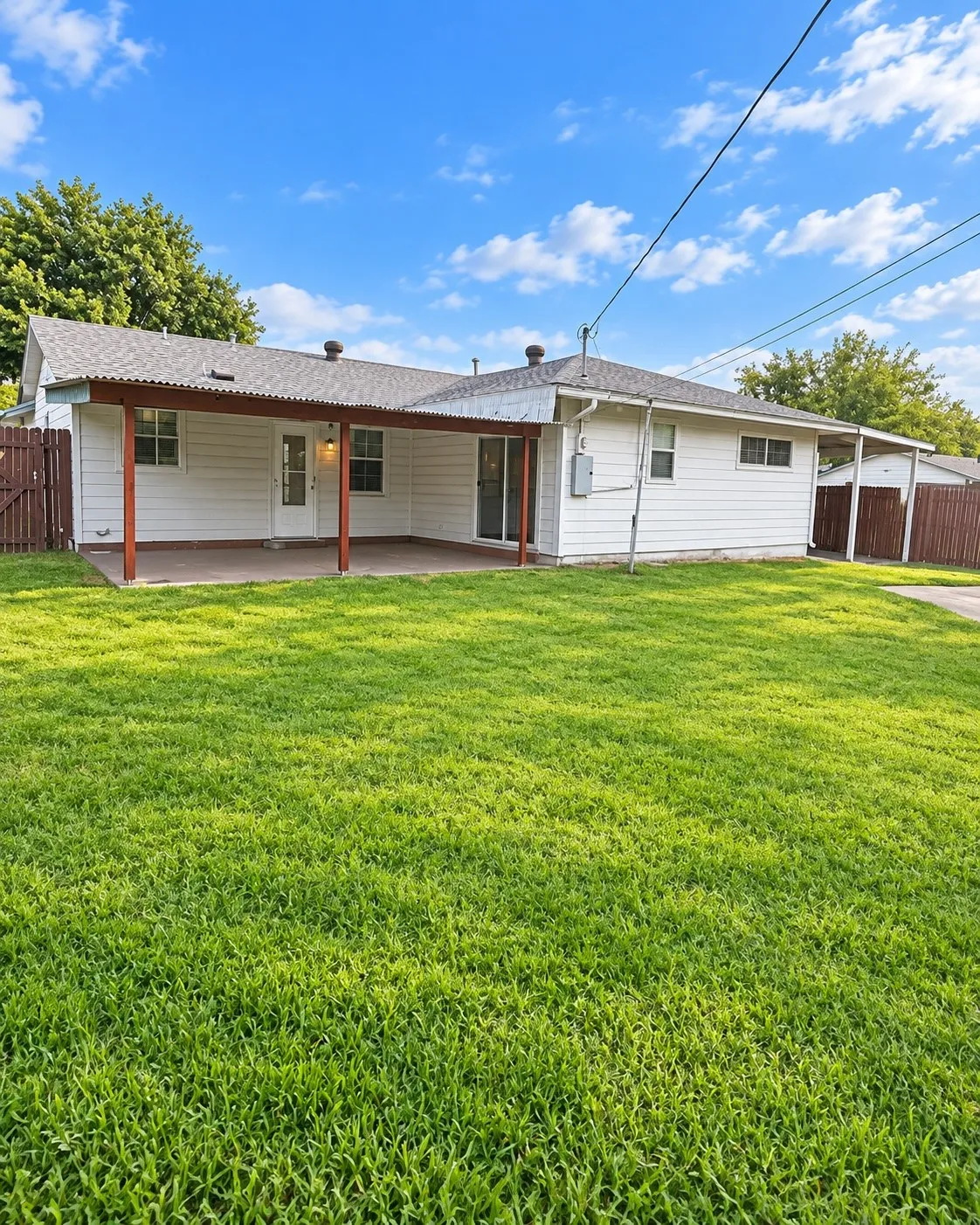Expansive rear yard featuring green grass, a covered patio with a concrete surface, a white exterior, and a wood privacy fence