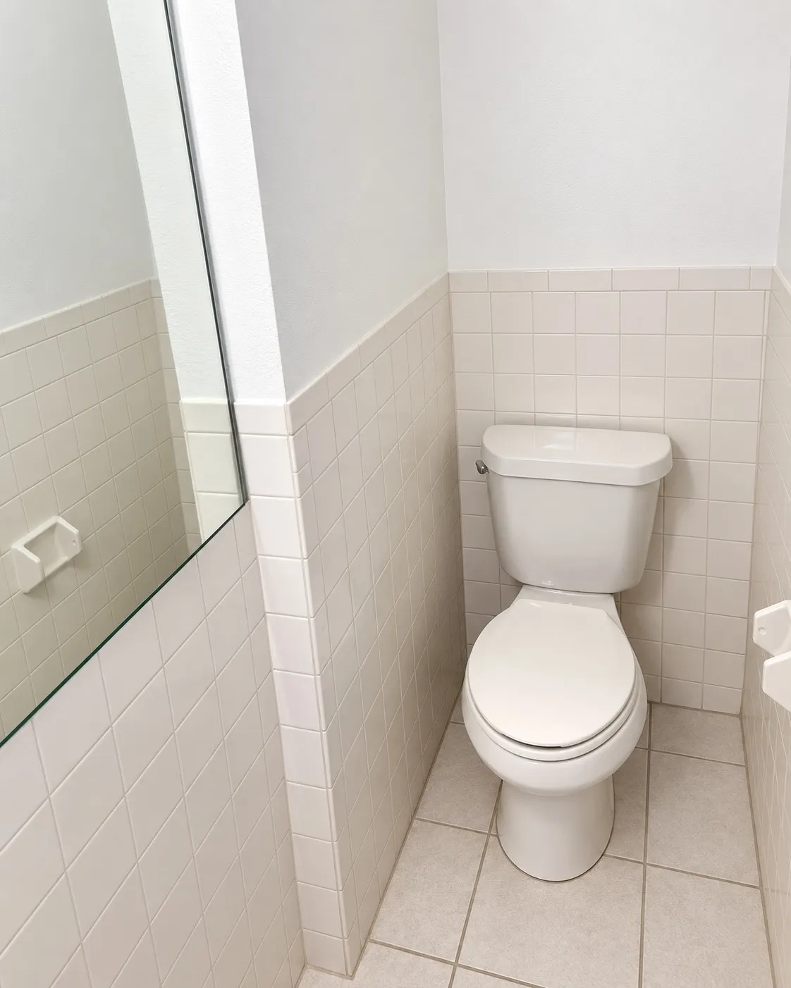White tile flooring, white wall-mounted toilet, and white ceramic wall tile