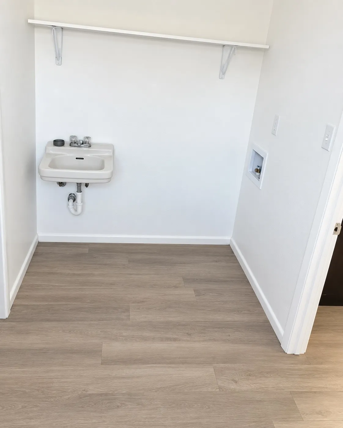 Utility room with wood-finish flooring, white walls, and a wall-mounted sink