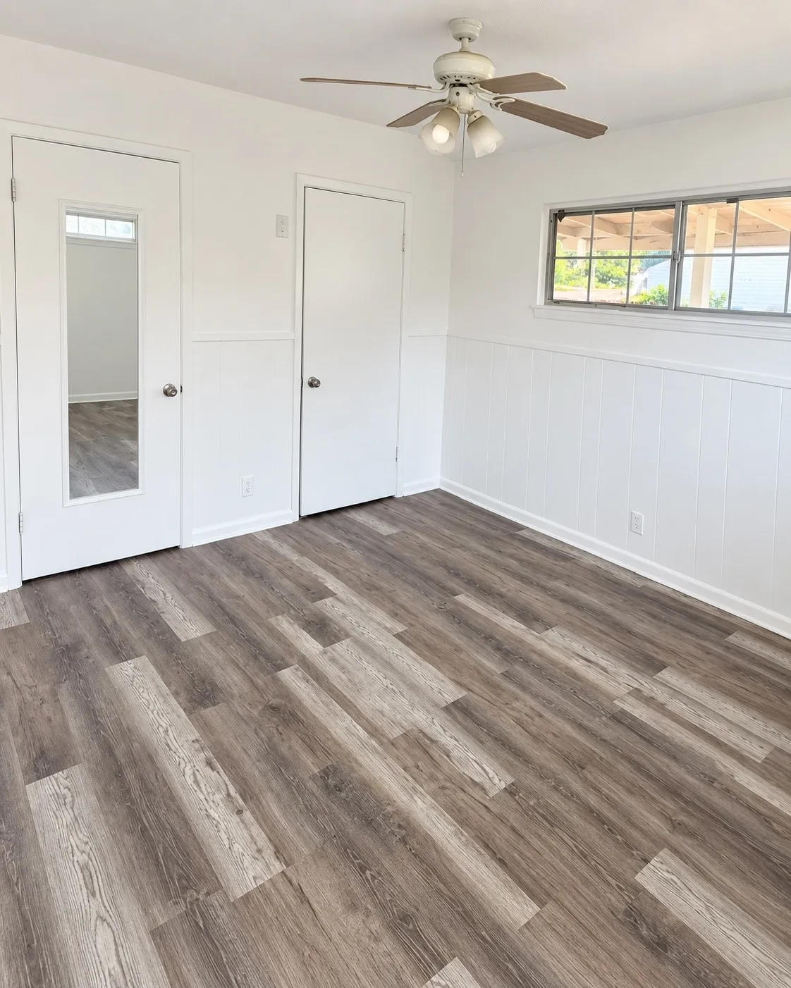 Wood-finish flooring, white paneling, ceiling fan with integrated lighting, and multiple windows