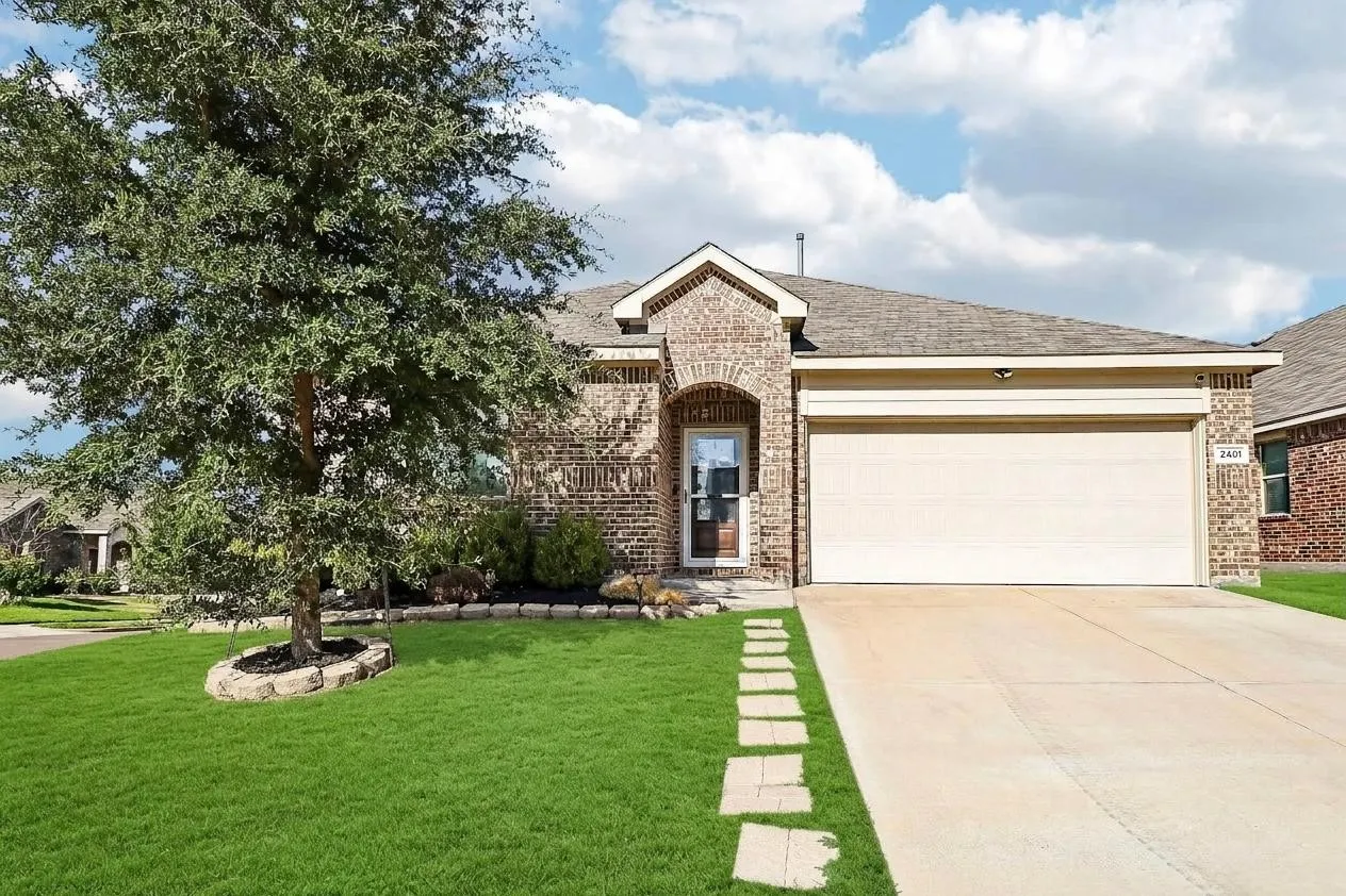Brick exterior with an arched entry, a two-car garage, a manicured lawn, and a paved walkway