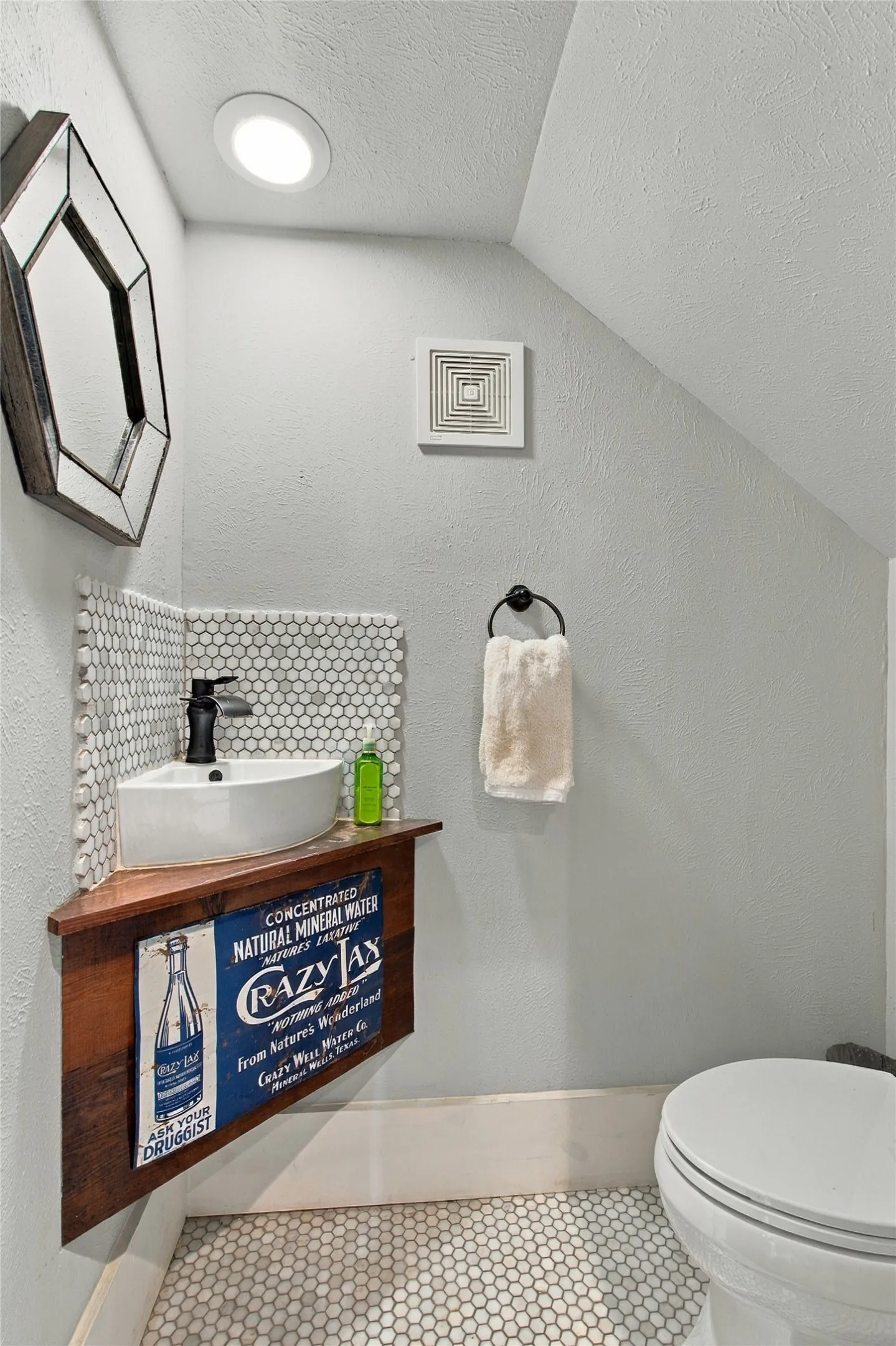 The hall bath with a corner-mounted basin sink set against white penny tile is tucked underneath the staircase for convenient access downstairs.
