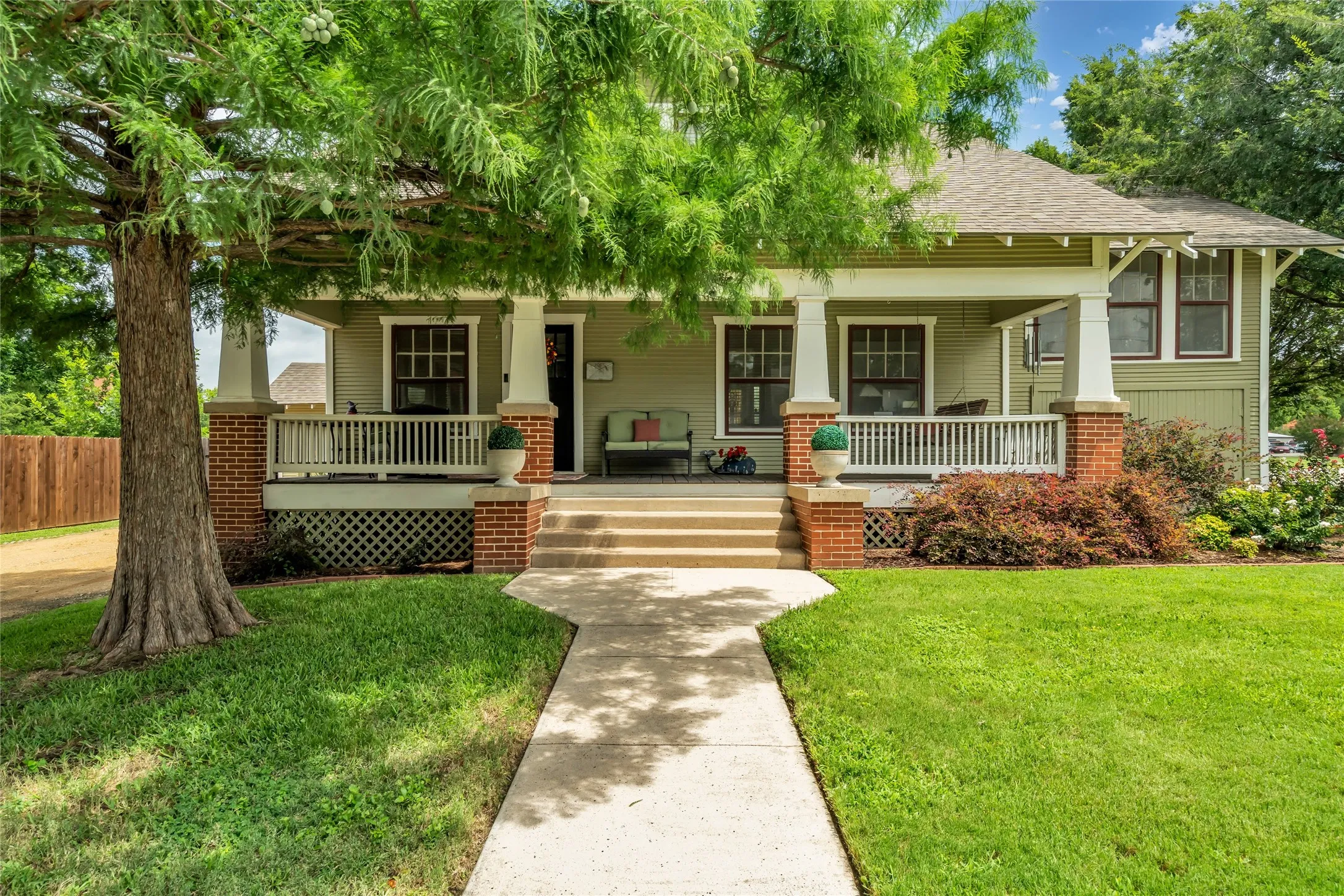 Craftsman-style exterior with a spacious front porch, large shade tree and a manicured lawn