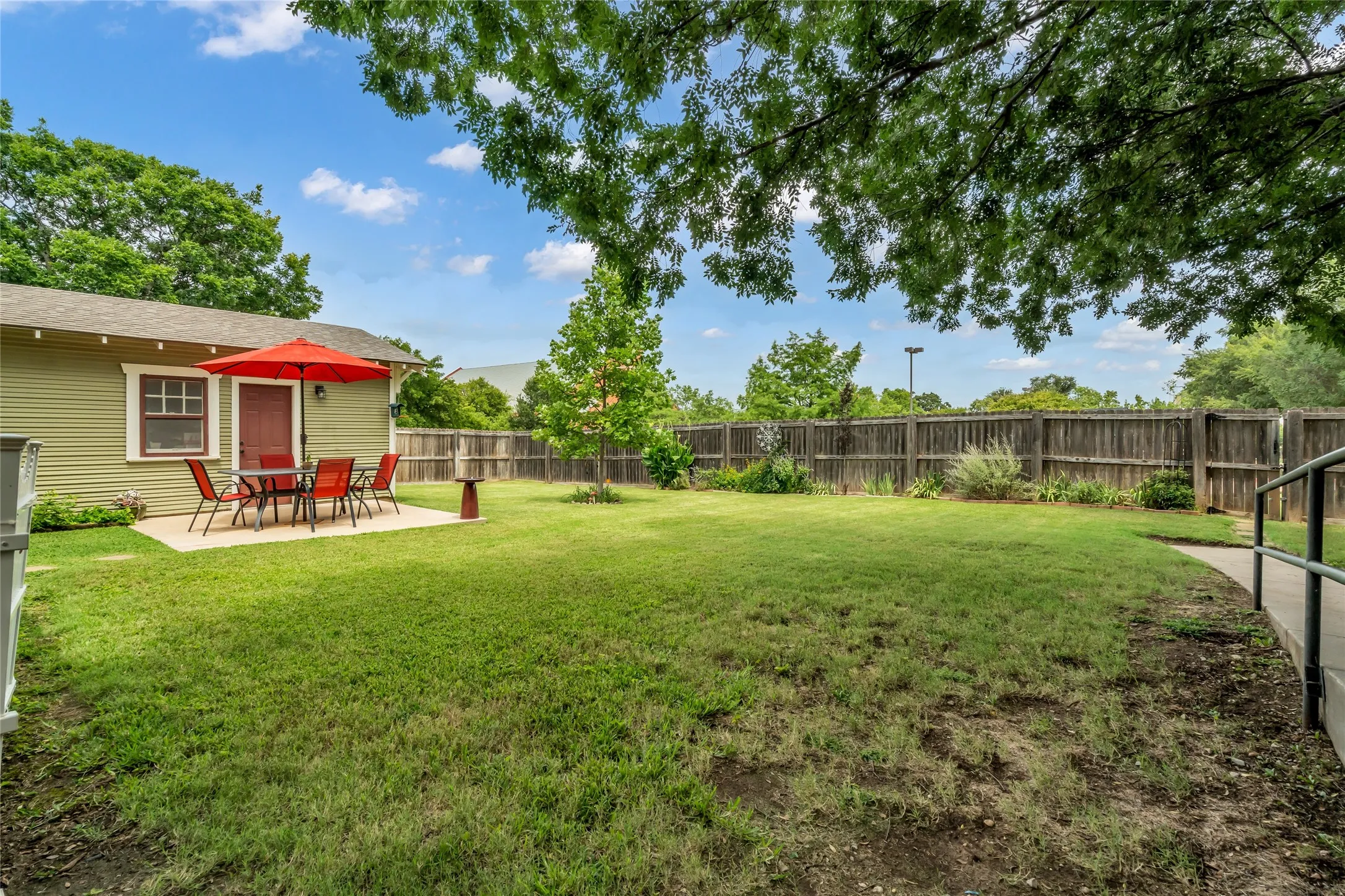 Expansive backyard featuring a lush lawn, mature trees, wood privacy fencing, and a concrete patio