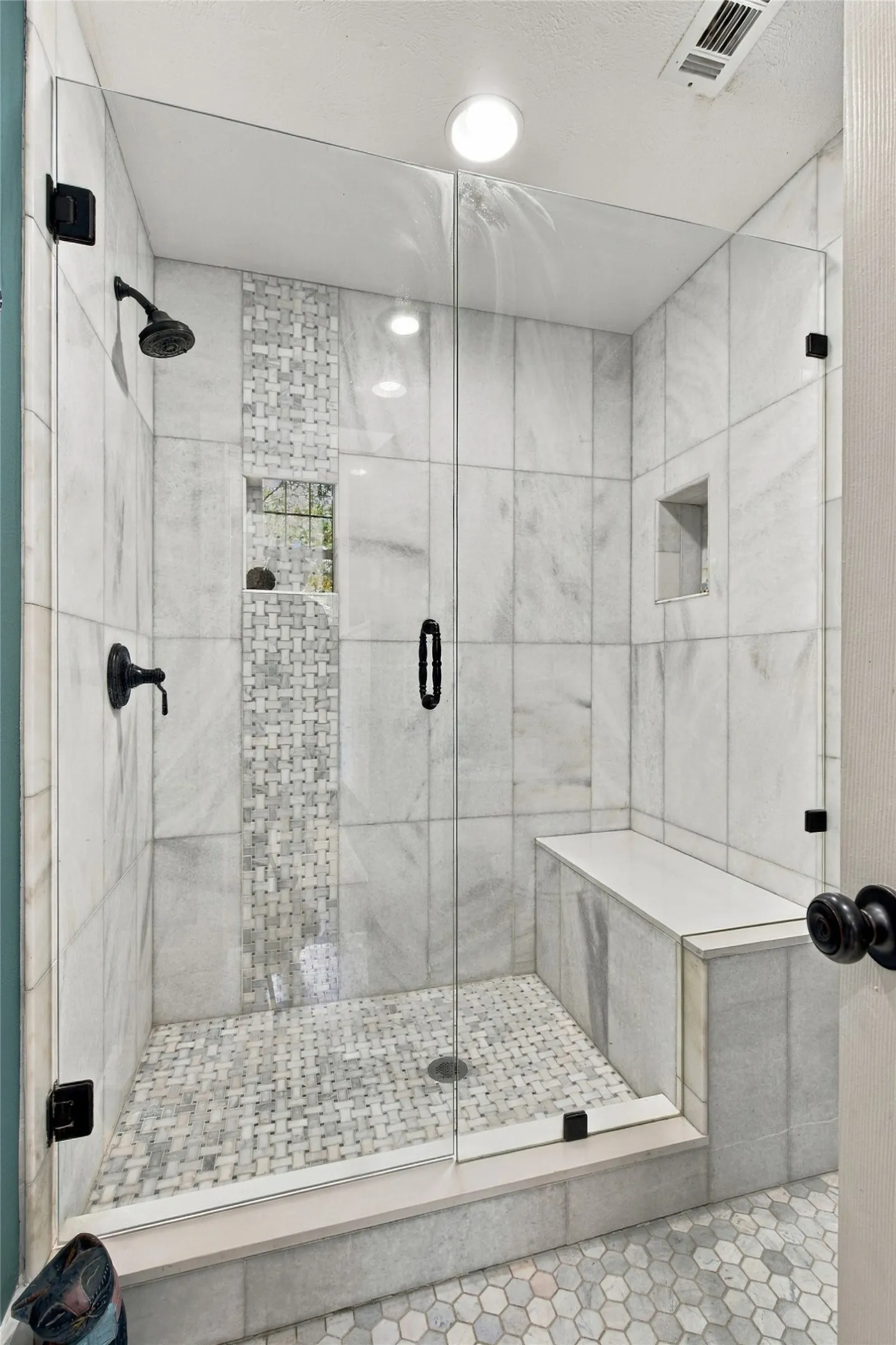 Glass-enclosed shower with a built-in bench, marble-finish tile walls, integrated shower niche, and a mosaic tile shower pan