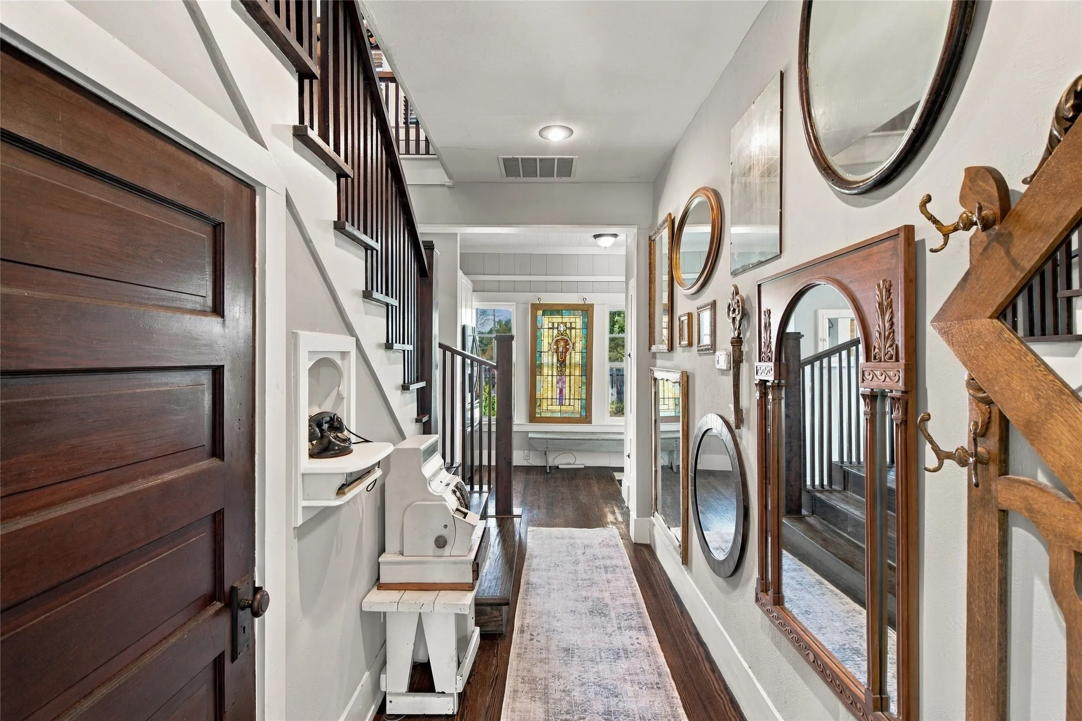 Hardwood flooring throughout the hallway, dark wood interior door with traditional hardware, wood staircase with dark balusters, and recessed ceiling lighting