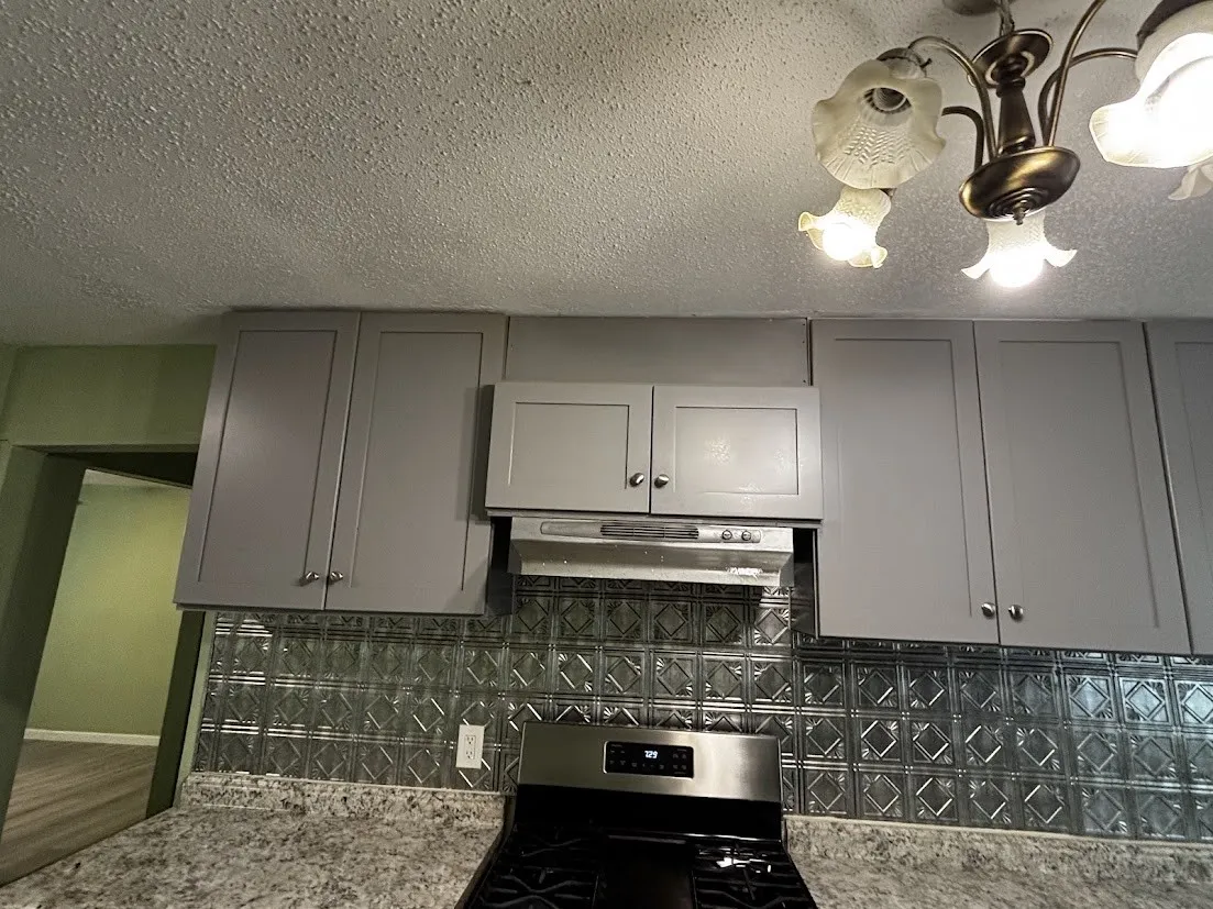 Galvanized metal backsplash, gray cabinetry, speckled countertops, and a modern range