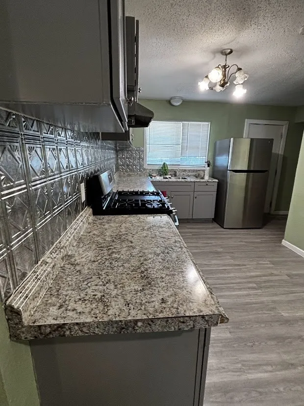Kitchen featuring stone-finish countertops, stainless steel appliances, a patterned tile backsplash, and wood-finish flooring