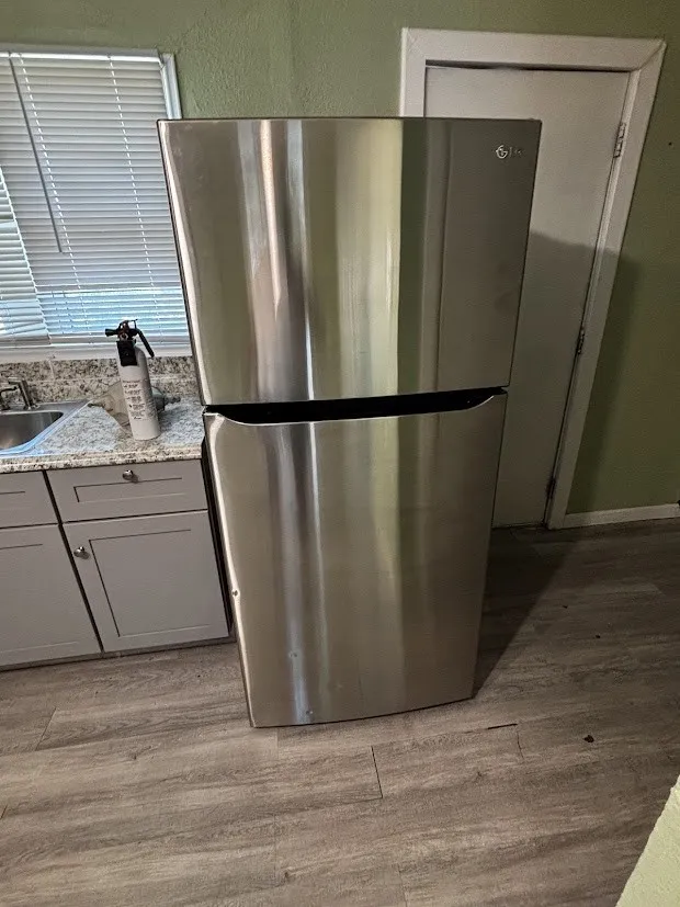 Stainless steel refrigerator, gray shaker-style cabinetry, speckled countertops, stainless steel sink, and wood-finish flooring