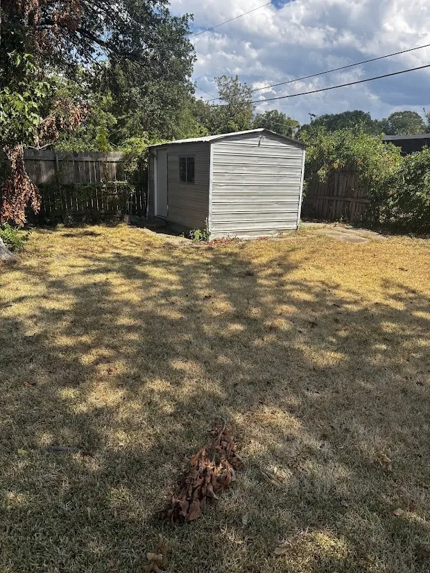 Fenced backyard featuring a metal shed with a window and a side door
