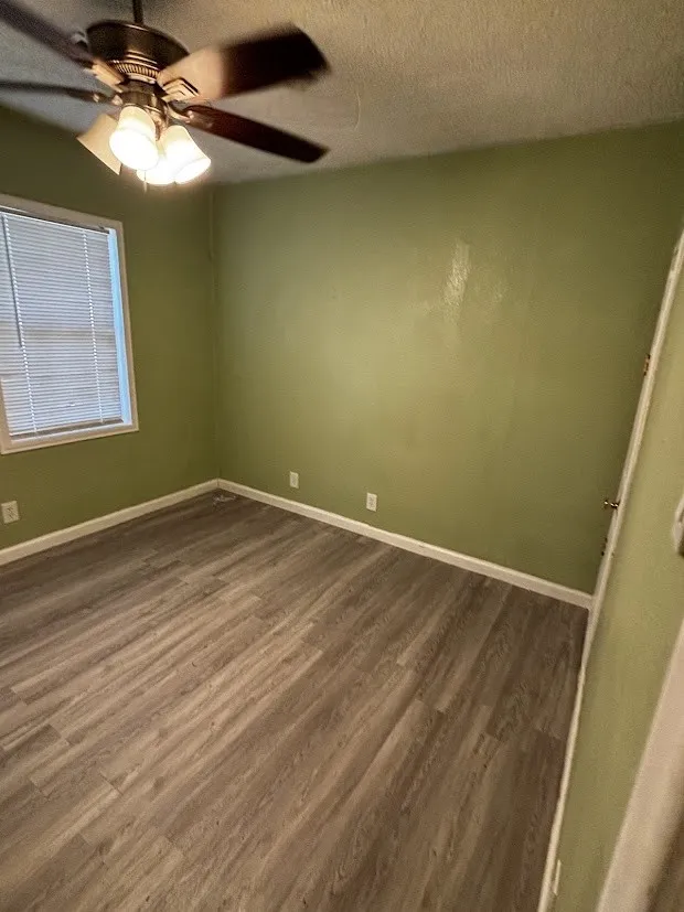 Wood-finish flooring, overhead ceiling fan with integrated lighting, window with blinds, and painted walls