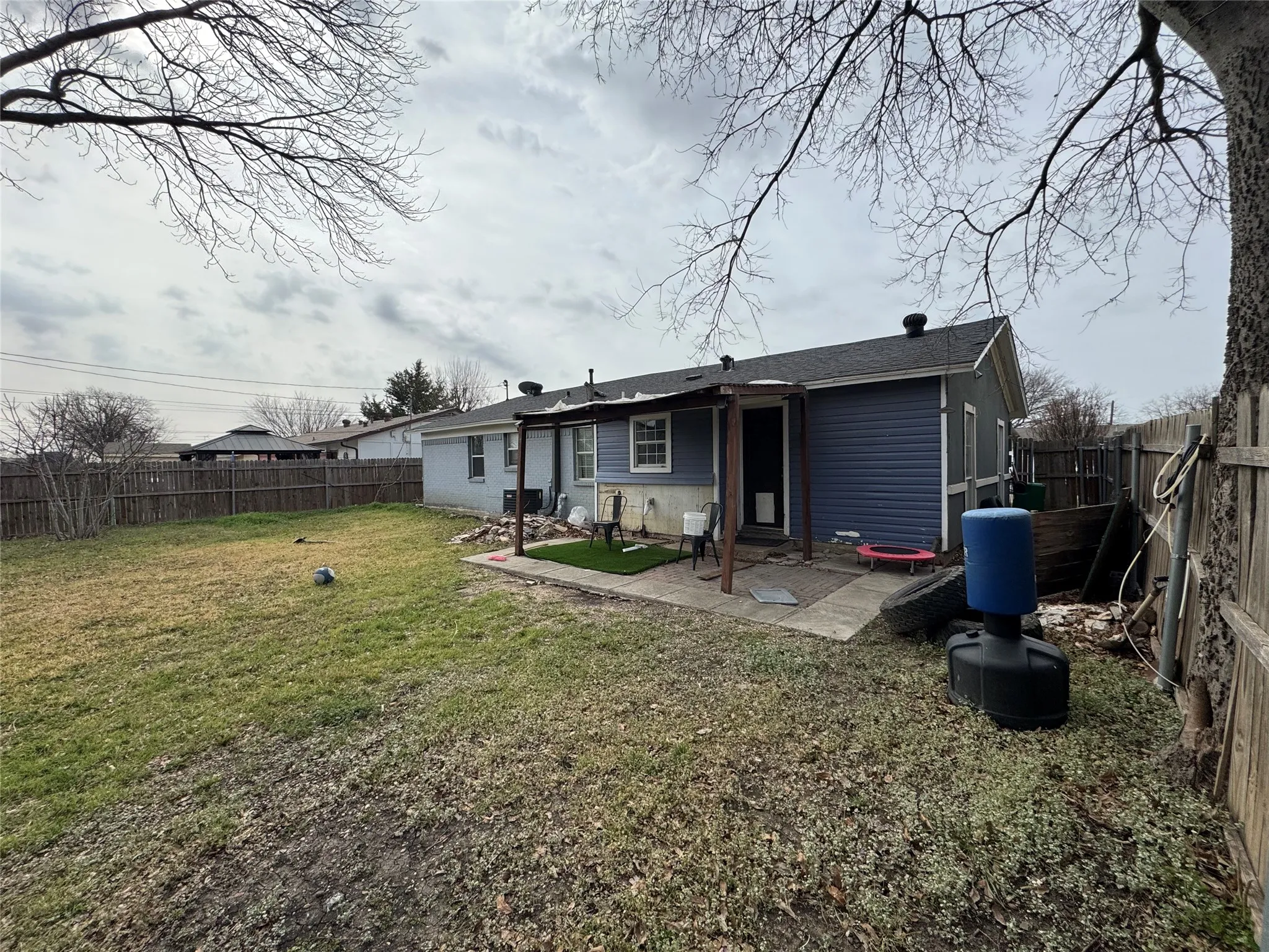 Rear exterior with blue siding, a covered patio, a concrete patio area, and a wood privacy fence