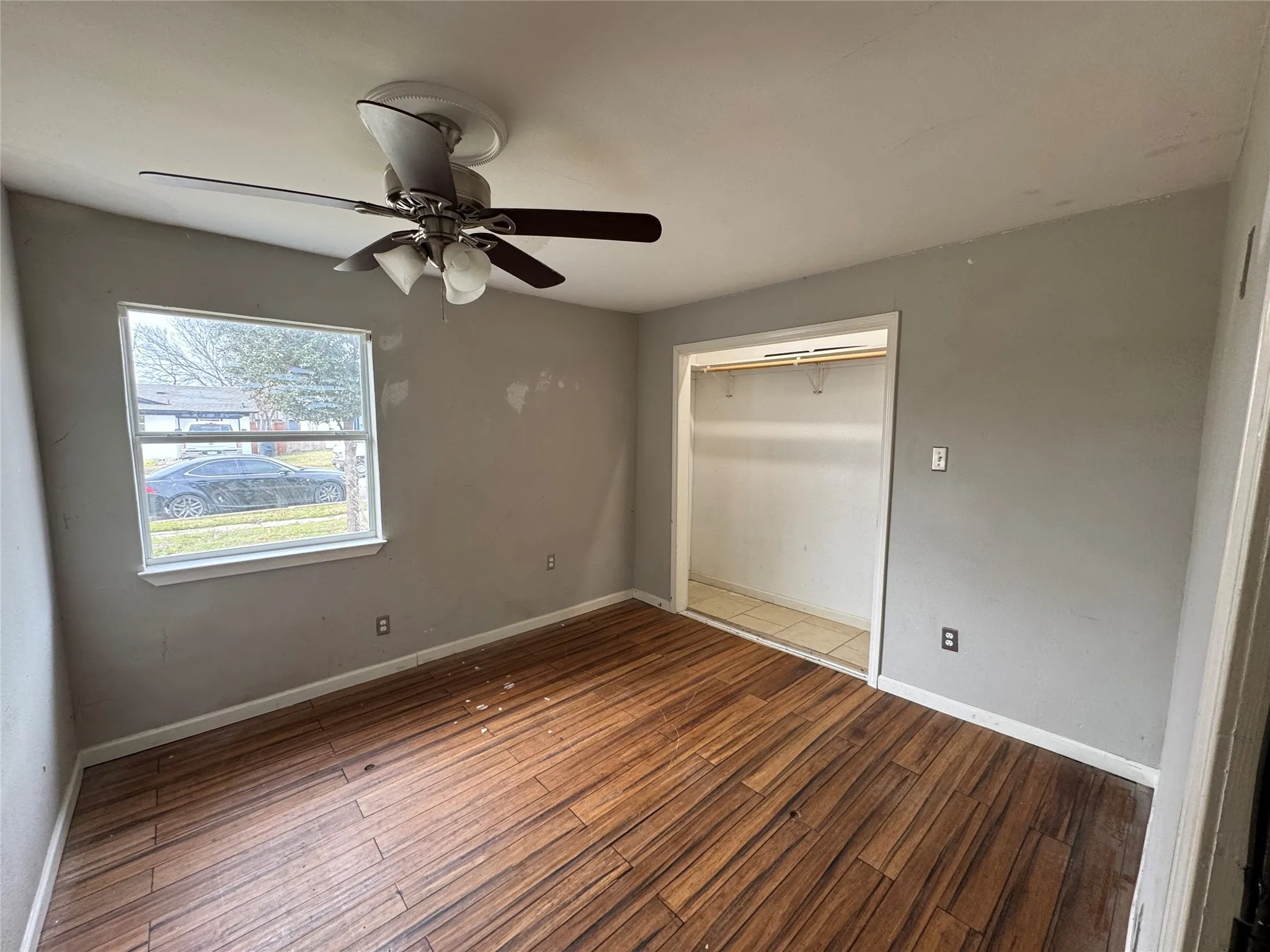 Wood-finish flooring, ceiling fan with integrated lighting, single window, and a closet with a hanging rod