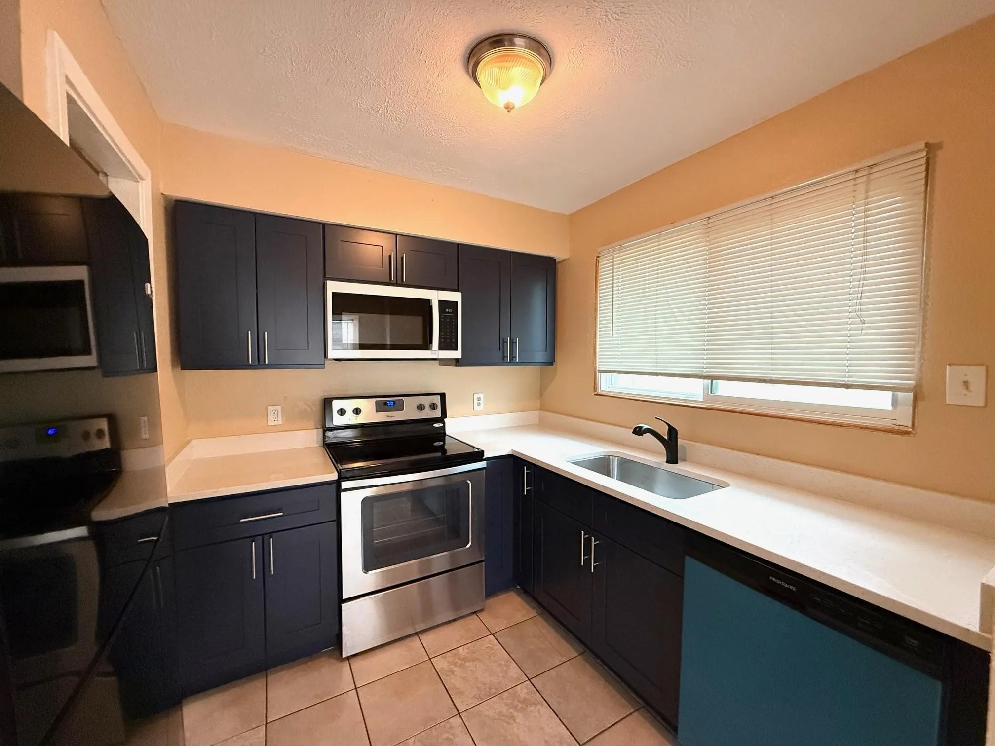 Galley kitchen featuring dark blue cabinetry, stainless steel appliances, light-toned countertops, and tile flooring