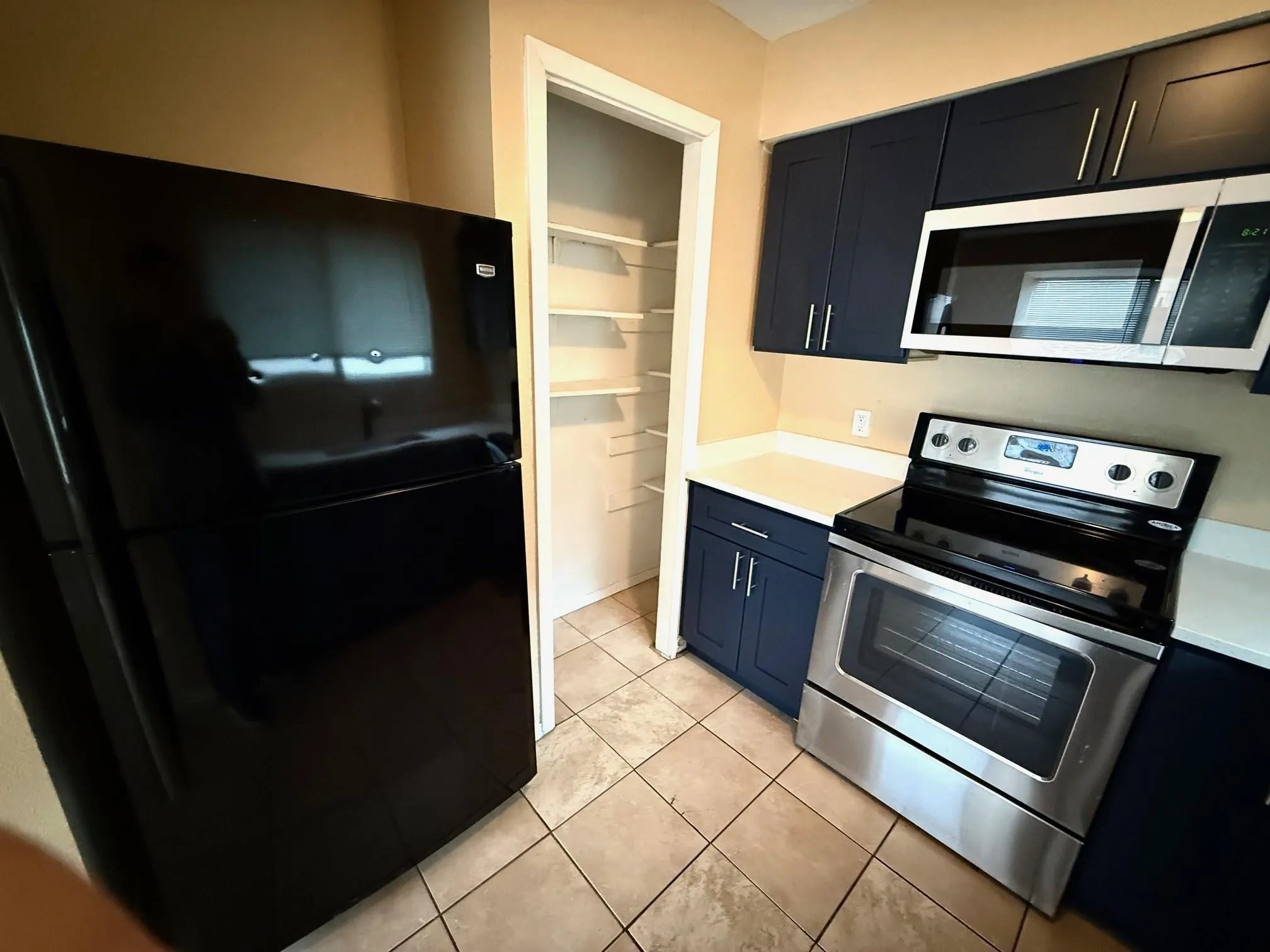 Kitchen featuring stainless steel range, built-in microwave, dark blue cabinetry, light countertops, and tile flooring