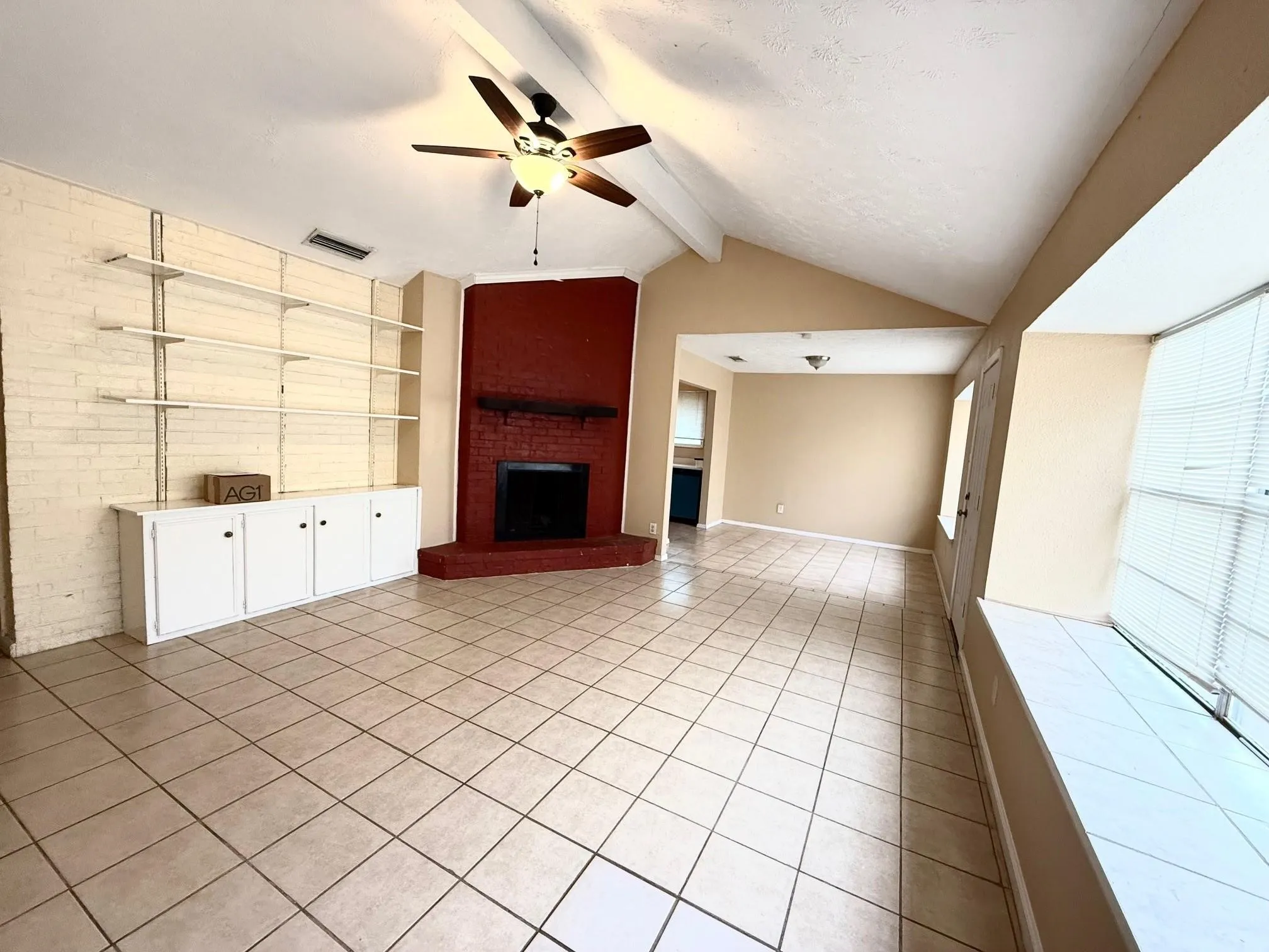 Vaulted ceiling with a ceiling fan, tiled flooring, brick accent wall with built-in shelving and cabinetry, and a brick fireplace