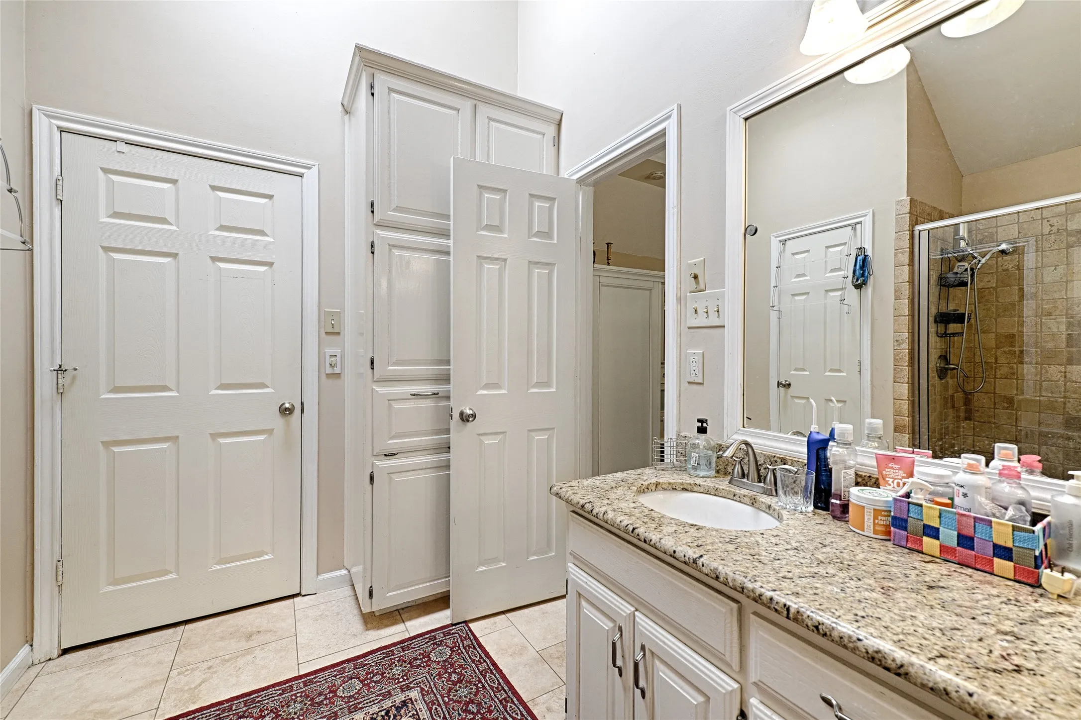 Granite countertop vanity with an undermount sink, a tiled shower, and extensive built-in storage cabinetry