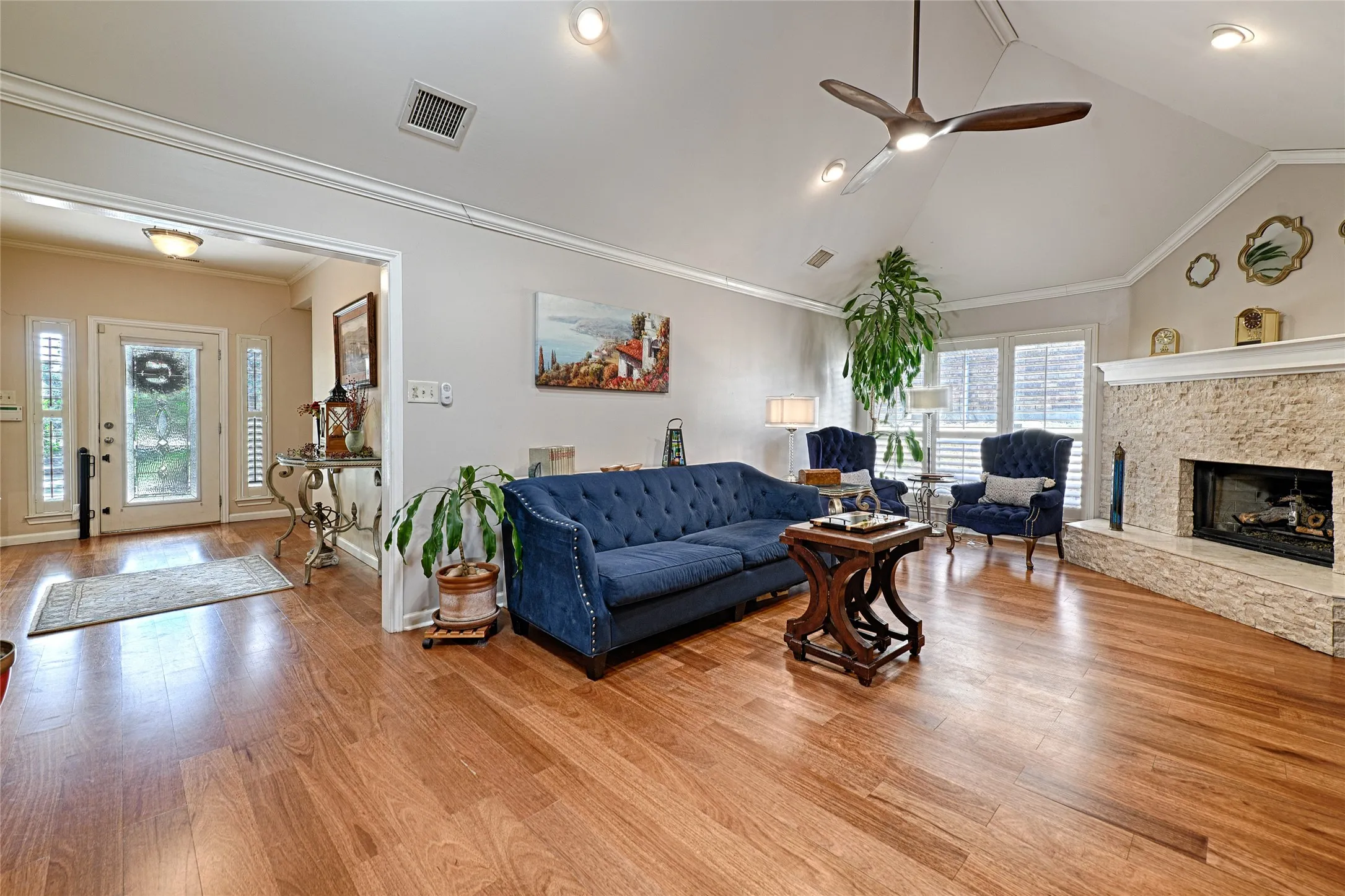 Vaulted ceiling with a ceiling fan, recessed lighting, wood-finish flooring, stone-clad fireplace, and window shutters