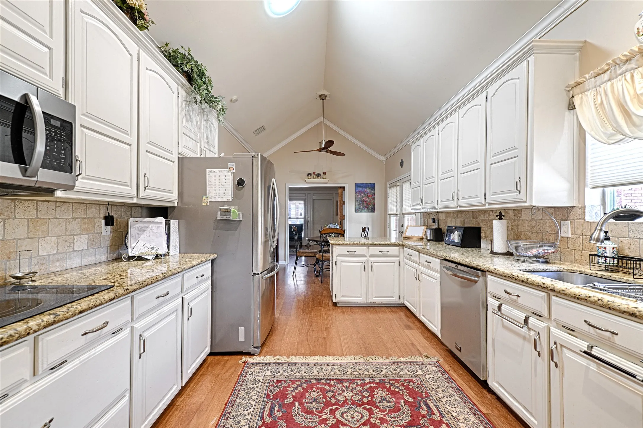 Vaulted ceiling kitchen featuring abundant white cabinetry, stainless steel appliances, granite-style countertops, and a tiled backsplash