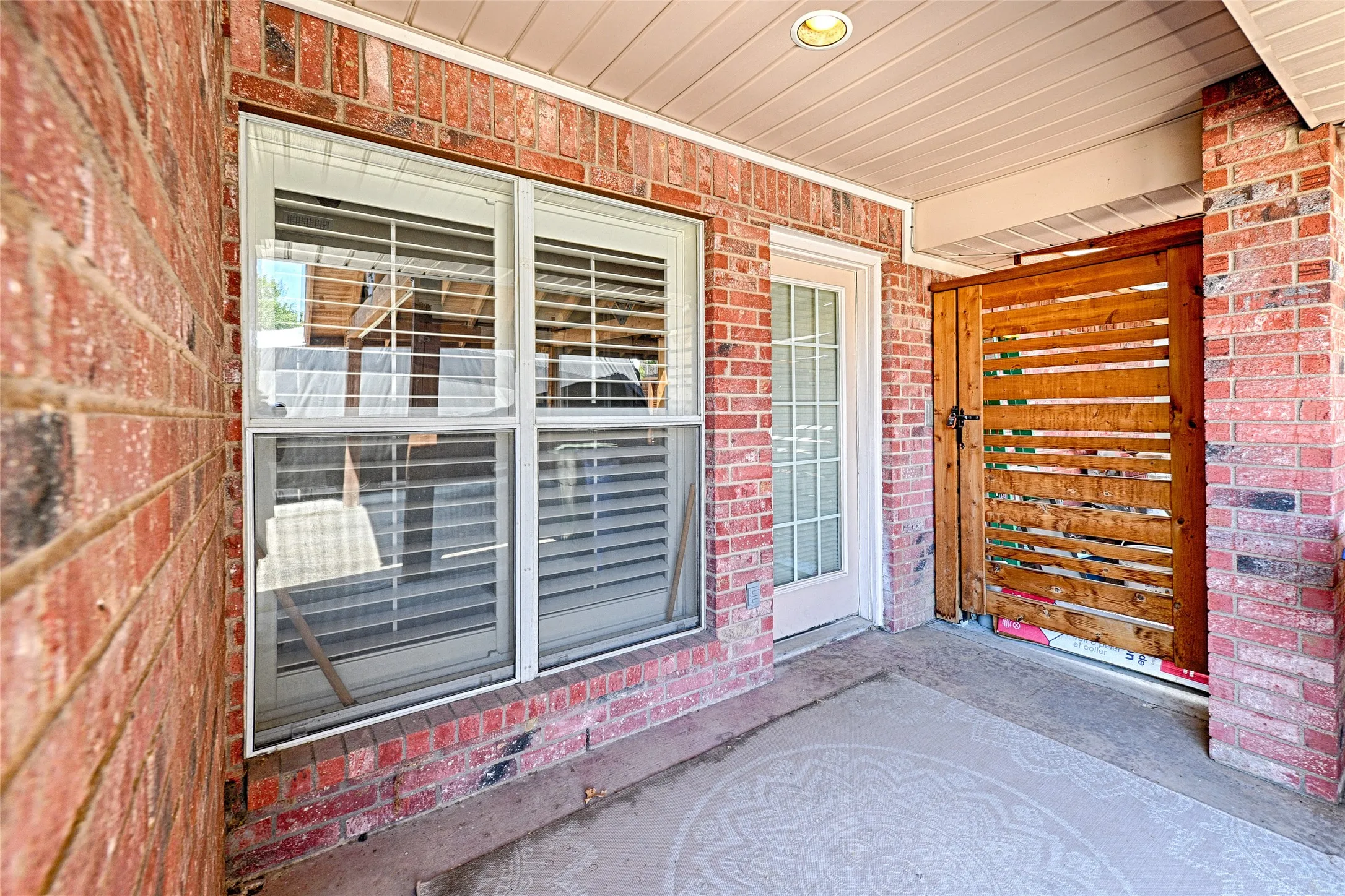 Brick exterior featuring a wood-slat privacy gate, white frame windows with louvered shutters, and a white paneled door