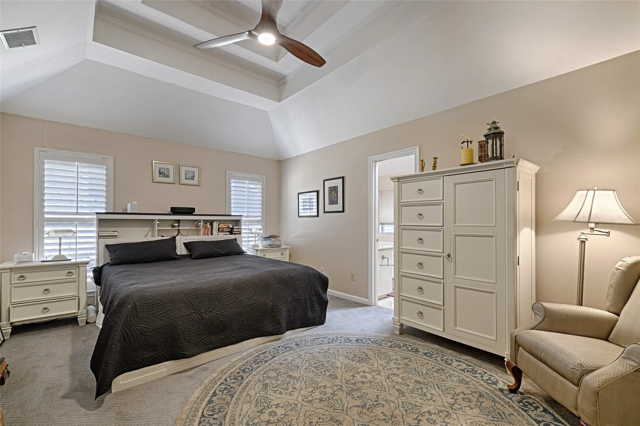 Tray ceiling with a modern ceiling fan, two windows with plantation shutters, and a built-in headboard with integrated shelving