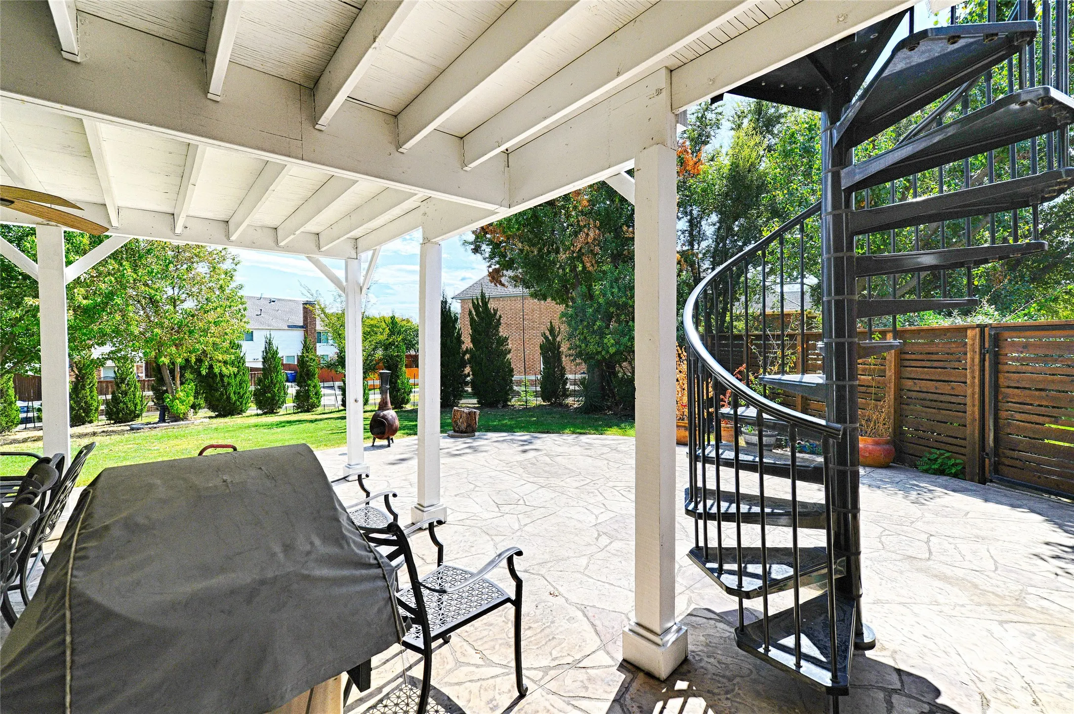 Covered patio featuring a ceiling fan, white support columns, and an exterior spiral staircase