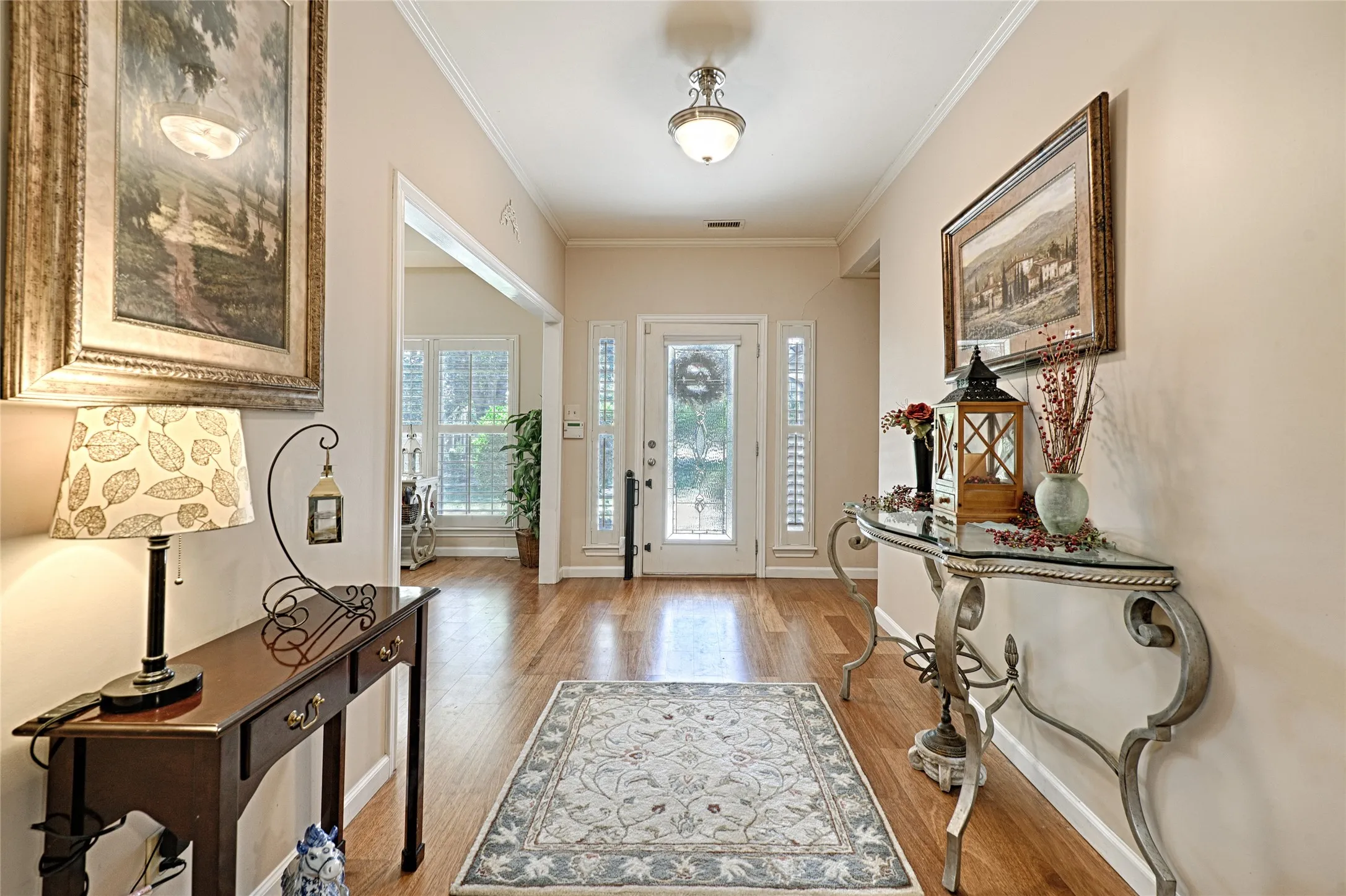Hardwood flooring in the entryway, crown molding, and a paneled front door with decorative glass inserts