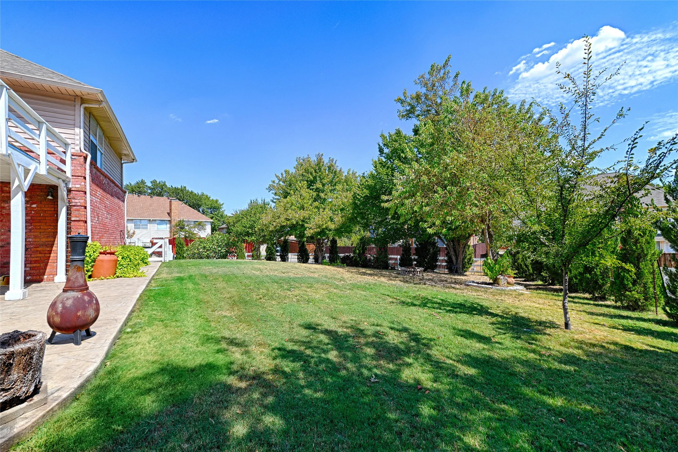 Expansive grassy yard with mature trees and a paved patio