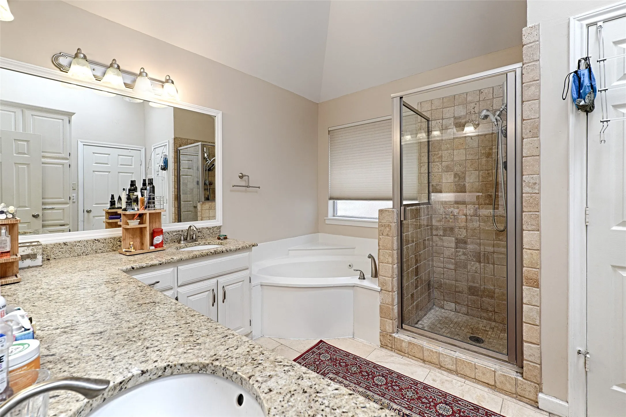 Dual vanity with granite countertops, a tiled walk-in shower with a glass enclosure, and a corner soaking tub