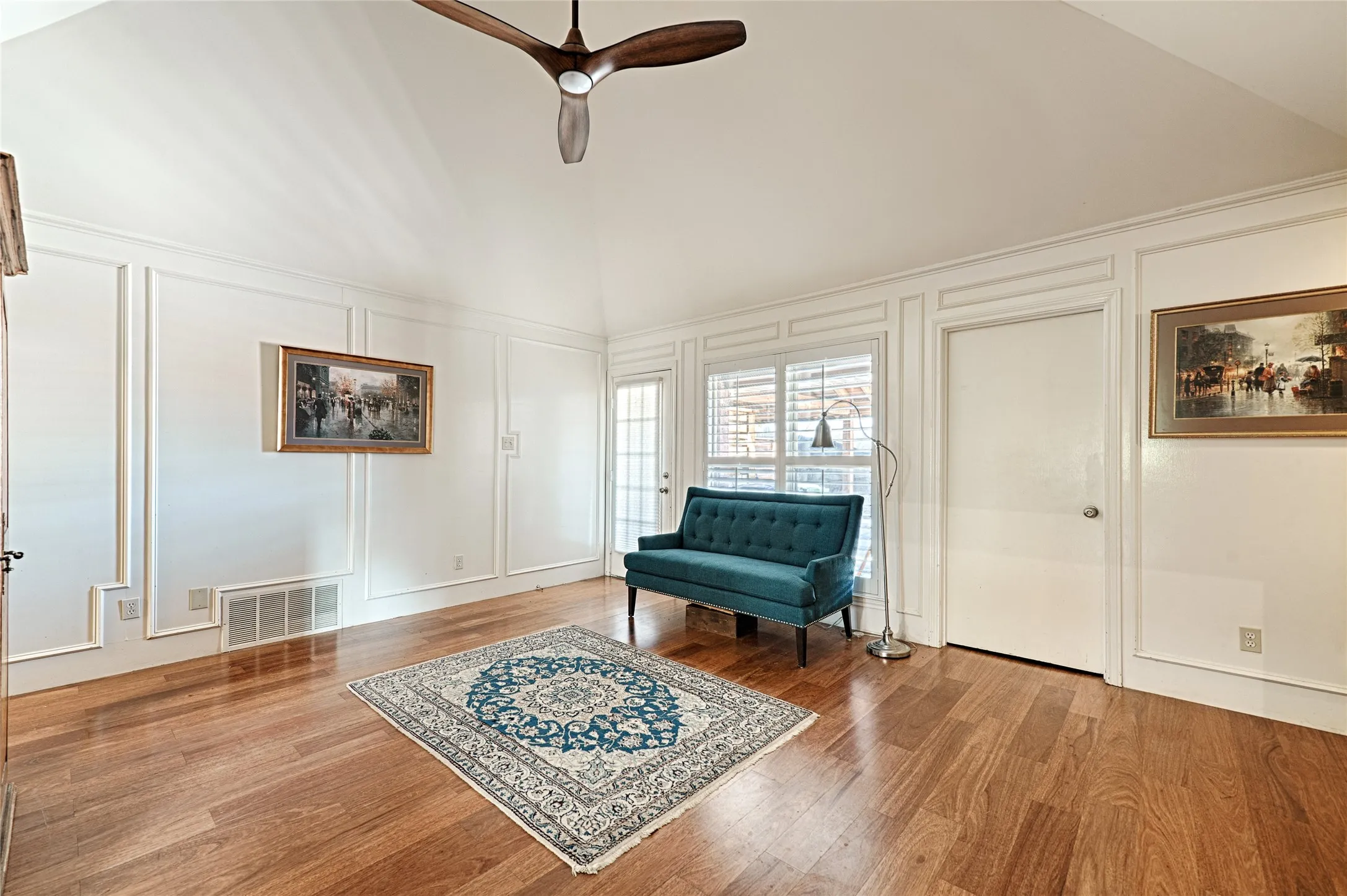 Vaulted ceiling, wood-finish flooring, paneled wall detailing, ceiling fan, and transom window