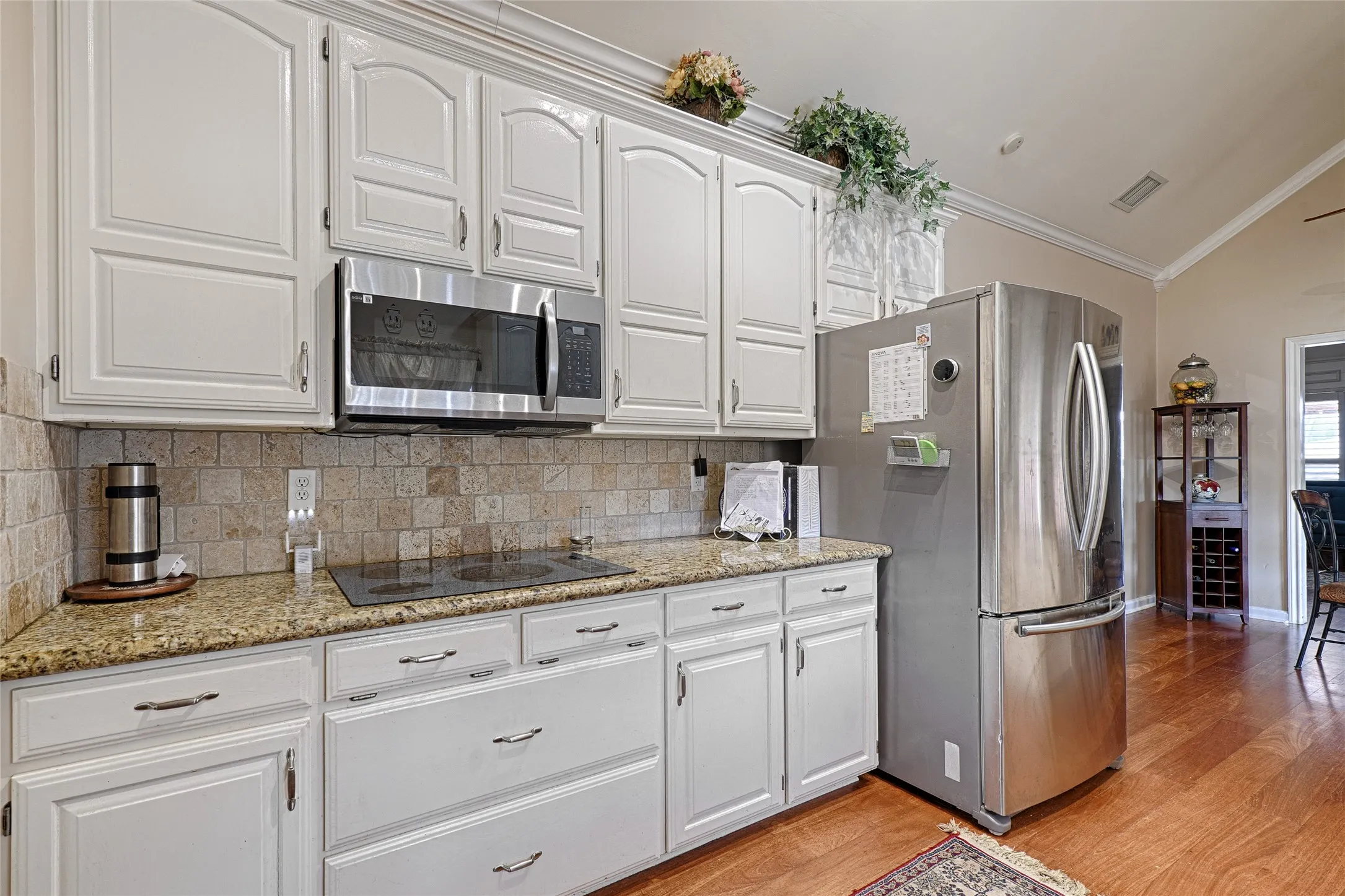 White cabinetry with curved panel doors, stone tile backsplash, wood-finish flooring, and built-in stainless steel appliances