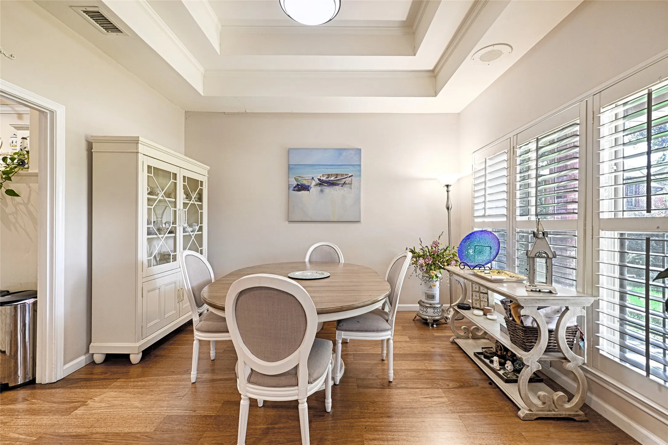 Tray ceiling with recessed lighting, wood-finish flooring, white plantation shutters, and a built-in display cabinet