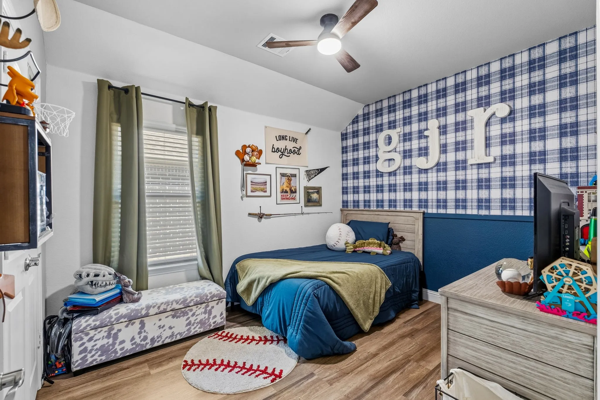 Wood-finish flooring, ceiling fan with integrated lighting, window with blinds, and decorative wall paneling