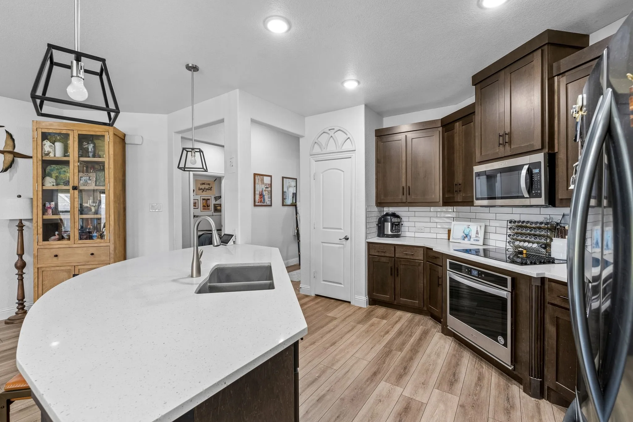 Spacious kitchen featuring an expansive island with an undermount sink, rich wood cabinetry, stainless steel appliances, and wood-finish flooring