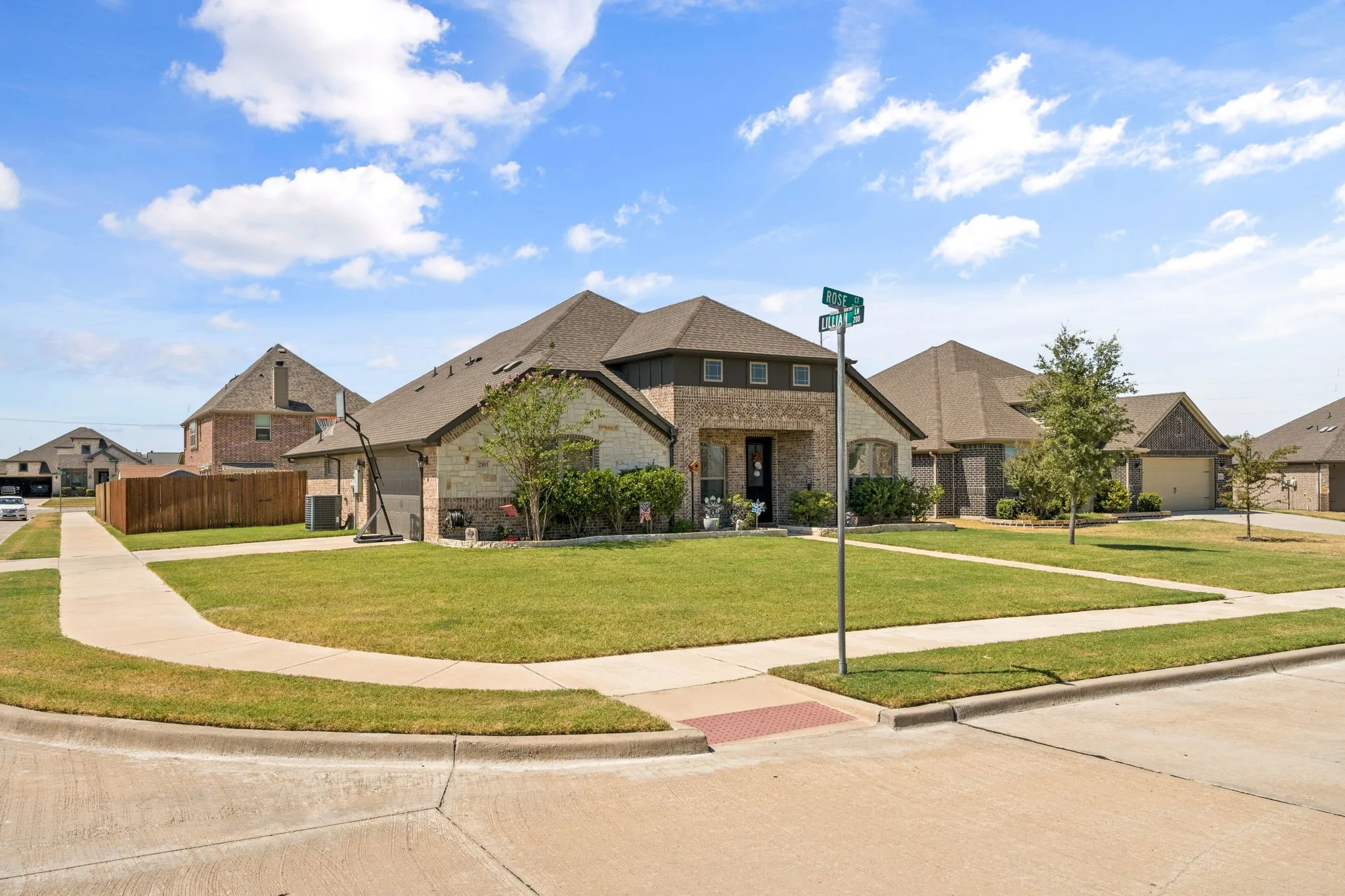 Brick and stone facade residence with a gabled roofline, established front lawn, and concrete sidewalks