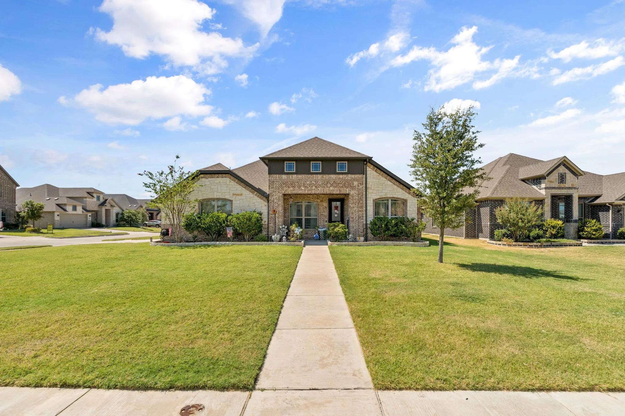 Brick and stone exterior, prominent front gable, integrated entryway, concrete walkway, and expansive front lawn