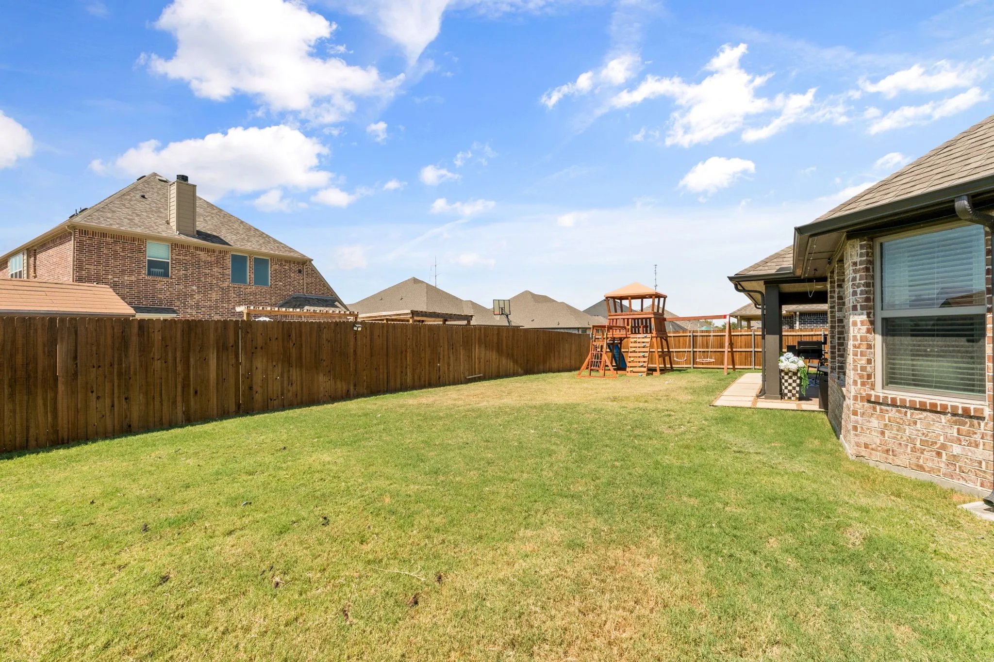 Expansive backyard featuring a manicured lawn, full privacy fencing, and a covered patio area
