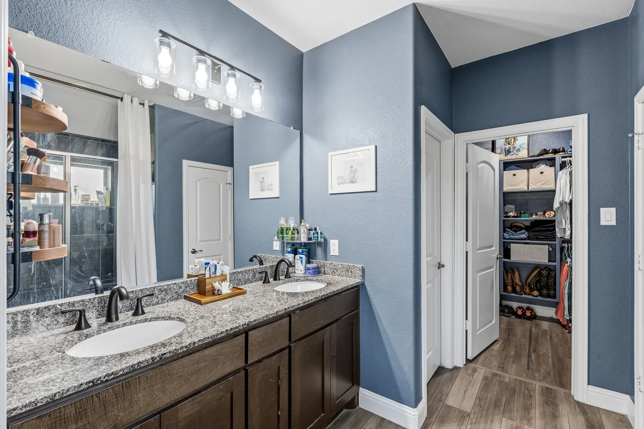 Dual vanity with granite-style countertop, matte black fixtures, wood-finish cabinetry, and an expansive wall mirror
