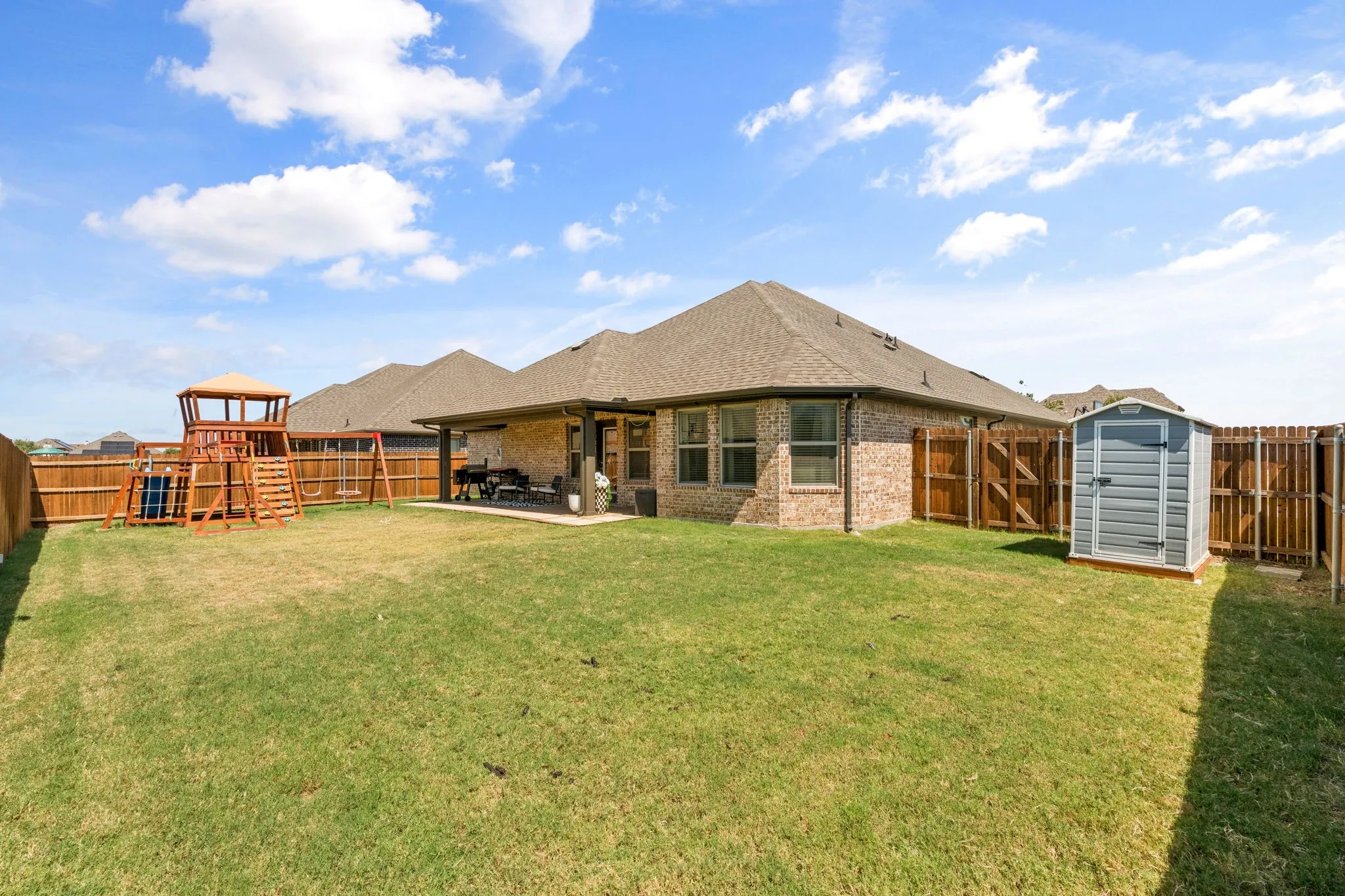 Expansive backyard featuring a covered patio, brick exterior, wood privacy fencing, and a storage shed