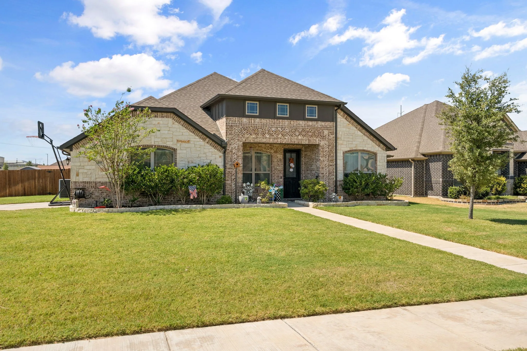 Brick and stone facade, gabled roofline, covered entry, front landscaping, and a concrete pathway