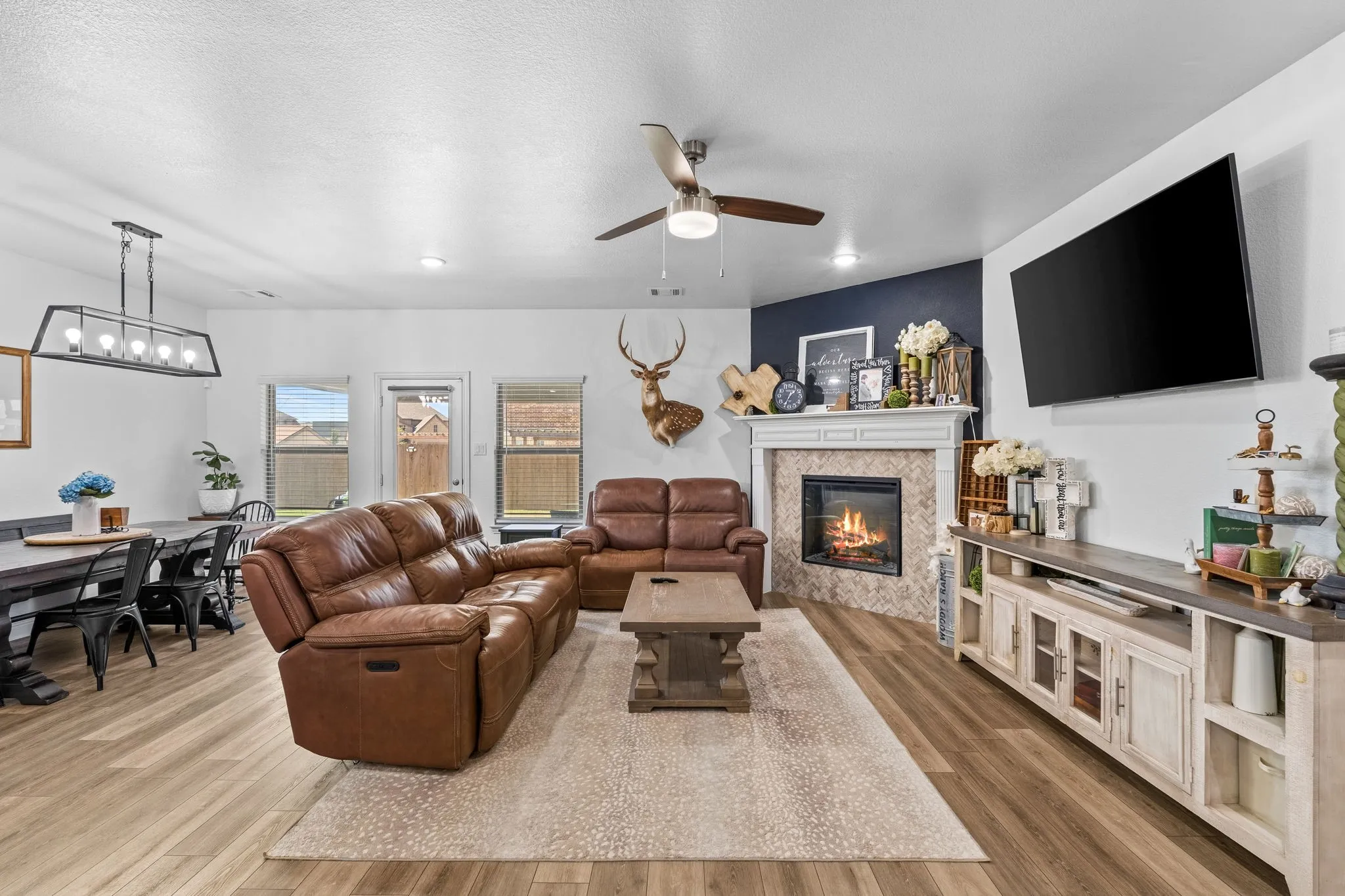 Wood-finish flooring throughout, a ceiling fan with integrated lighting, and a corner fireplace with a tiled surround and mantel