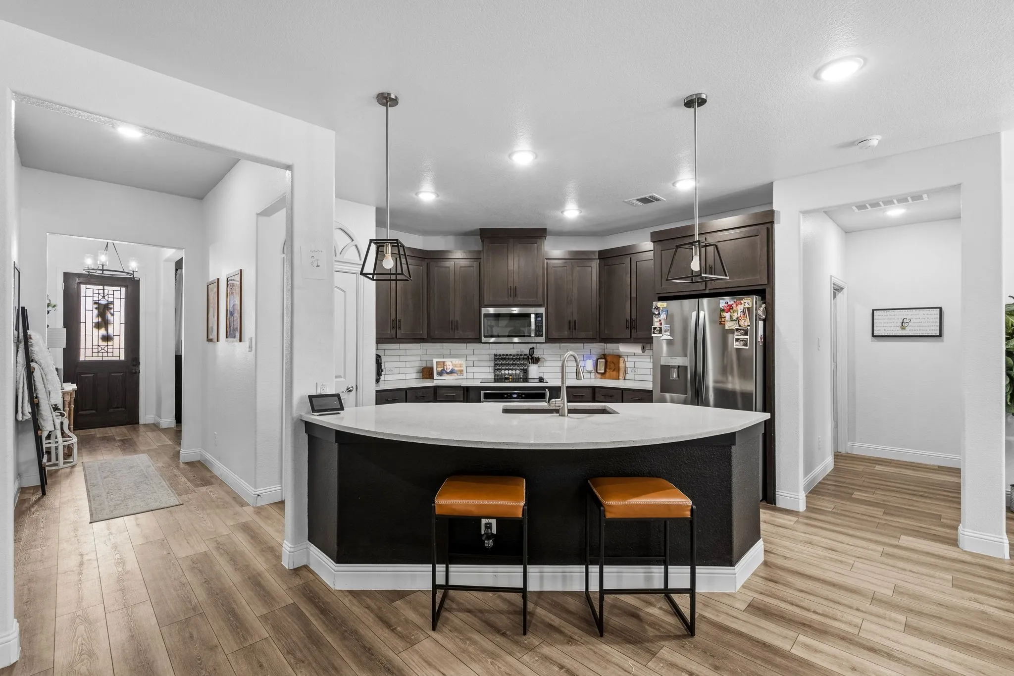 Kitchen featuring wood-finish flooring, dark wood cabinetry, a subway tile backsplash, stainless steel appliances, and a curved island with a light-colored countertop