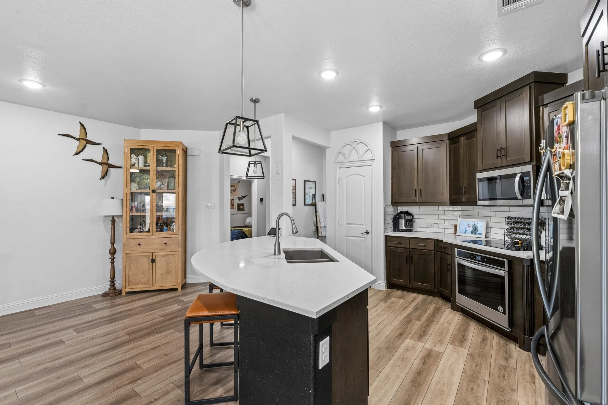 Kitchen featuring wood-finish flooring, dark wood cabinetry, white subway tile backsplash, stainless steel appliances, and an island with a white countertop