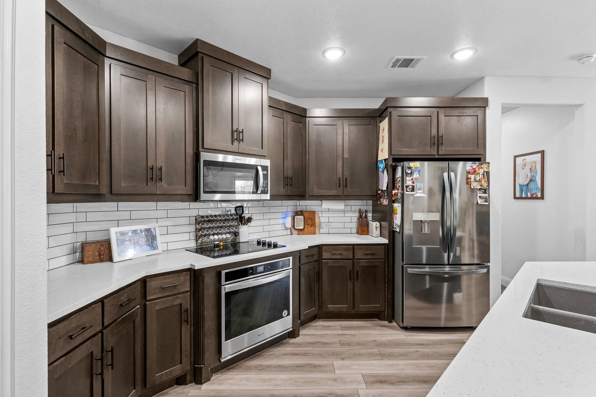 Kitchen featuring wood-finish cabinetry, stainless steel appliances, white subway tile backsplash, and light-toned countertops