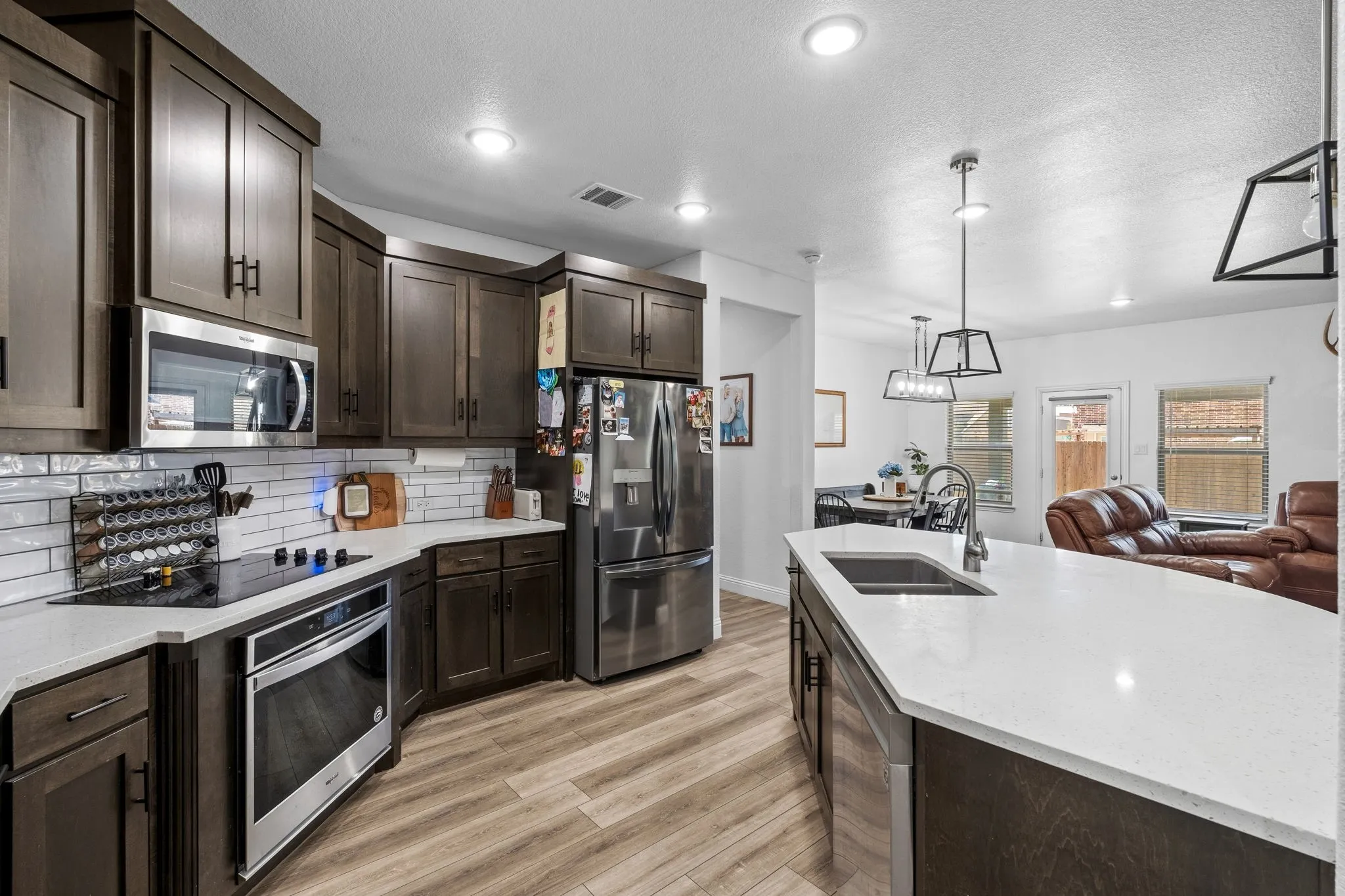 Kitchen featuring wood-finish flooring, dark wood cabinetry, white subway tile backsplash, and stainless steel appliances