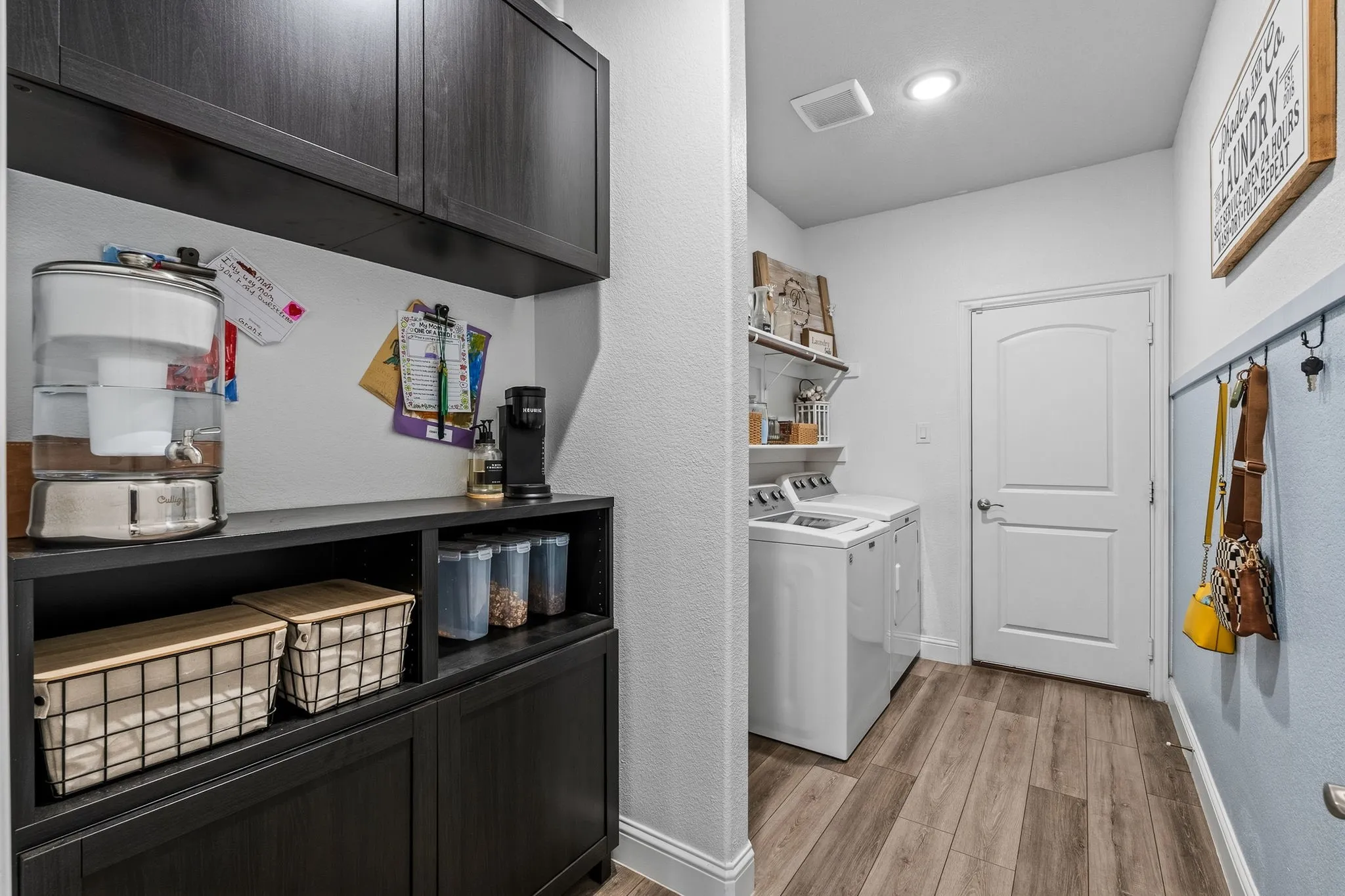 Laundry area featuring wood-finish flooring, built-in shelving, and dark wood-finish cabinetry