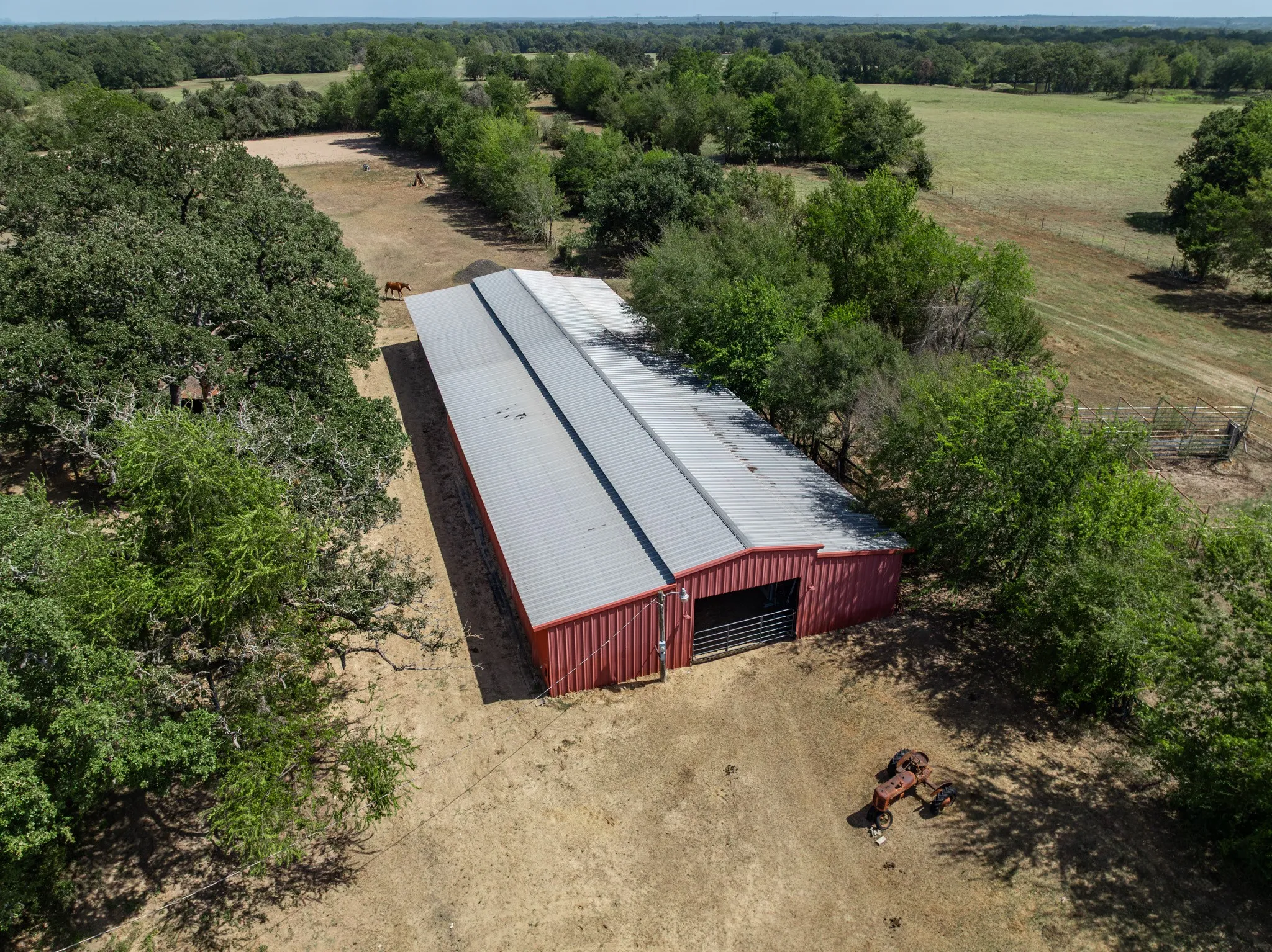 Red metal barn with a silver metal roof, surrounded by mature trees and open land