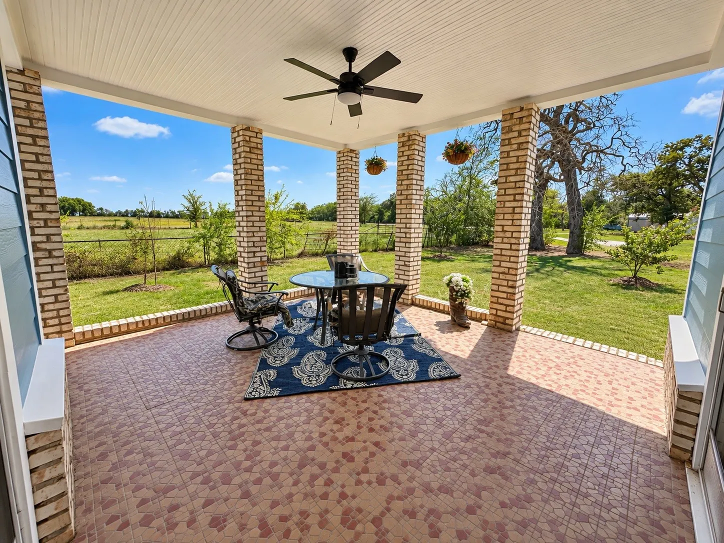 Covered patio with brick columns, patterned tile flooring, beadboard ceiling, and ceiling fan