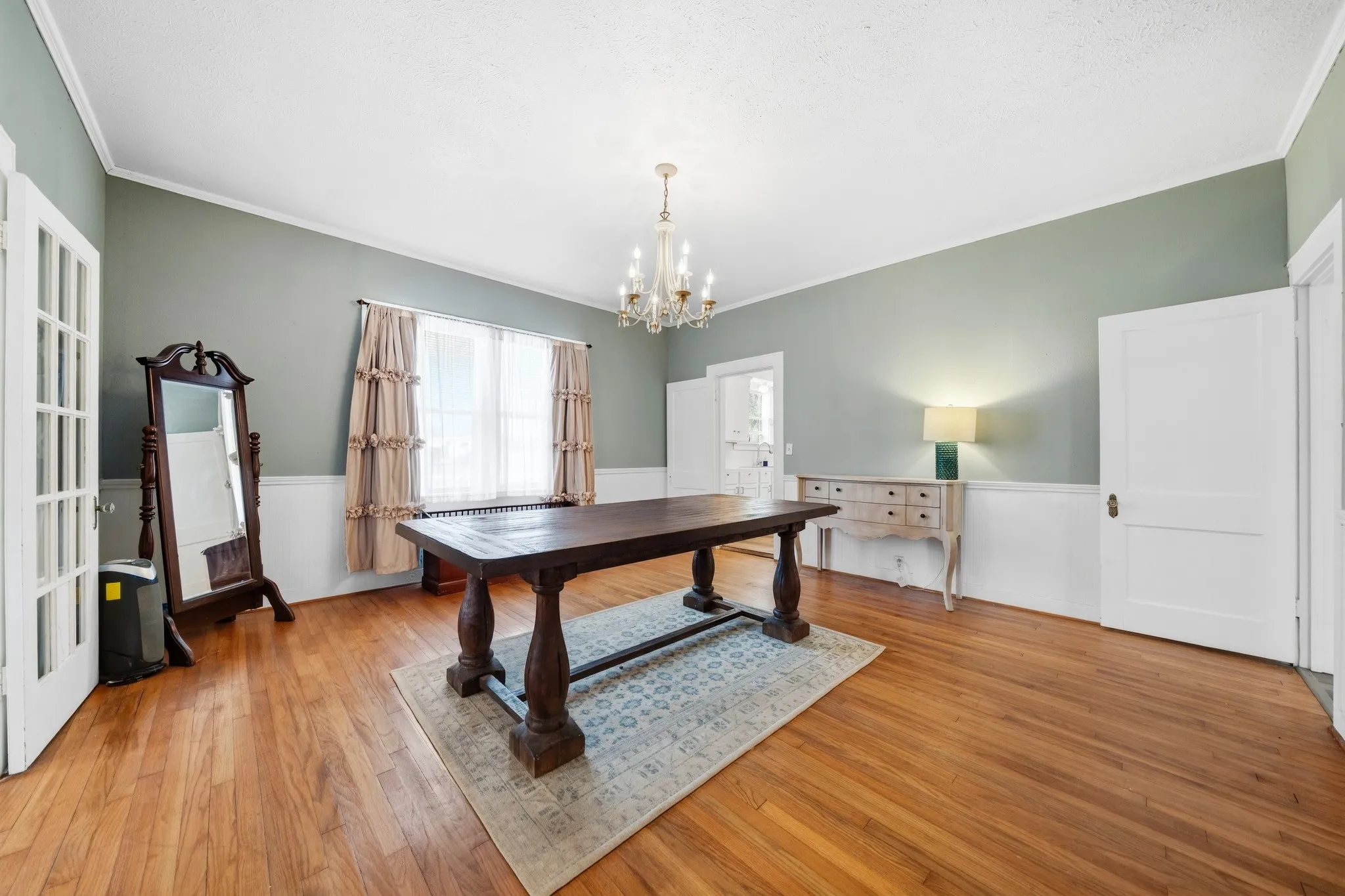 Hardwood flooring, crown molding, white wainscoting, and a window with natural light