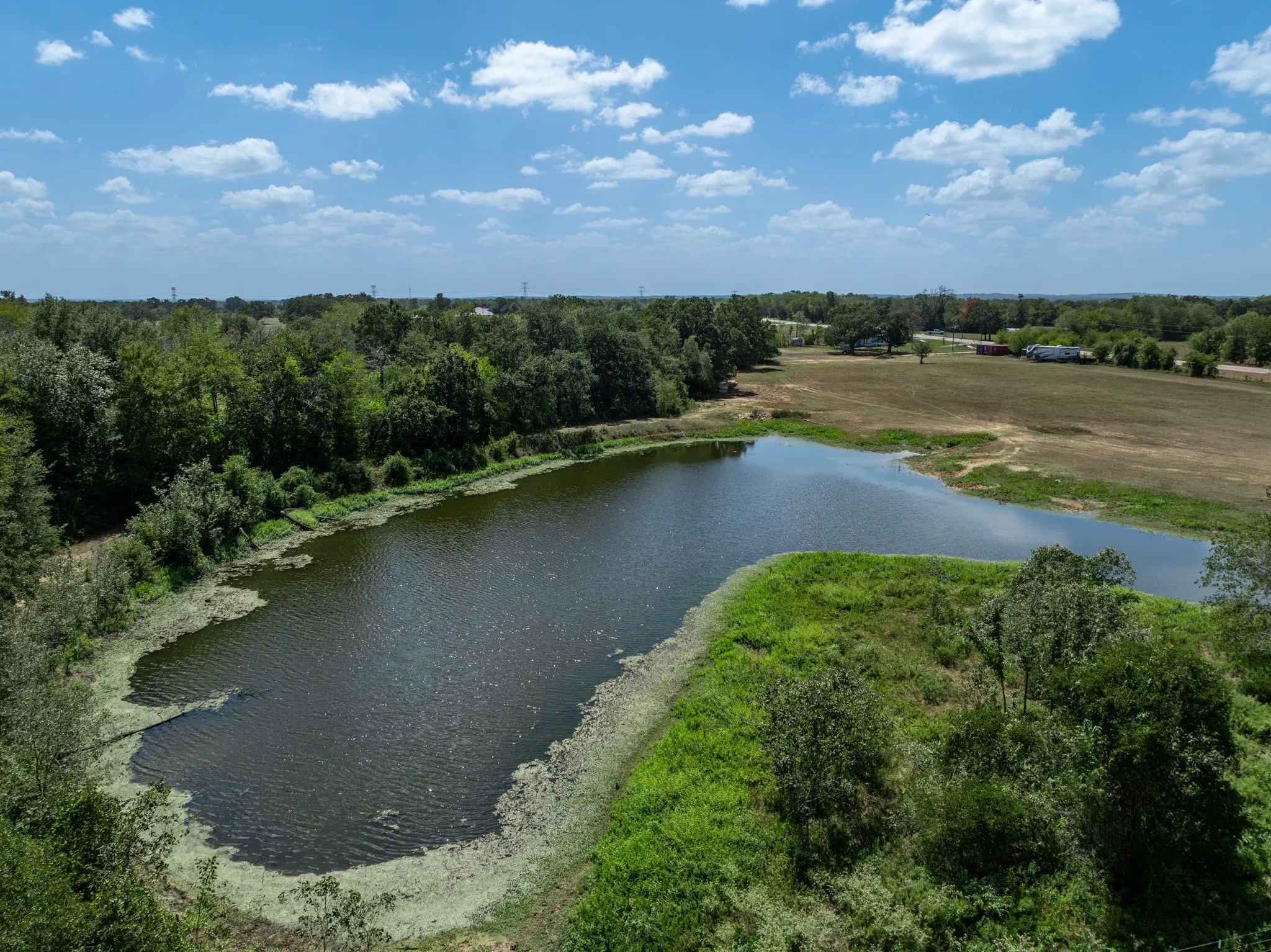 Expansive outdoor space featuring a large pond and surrounding wooded areas